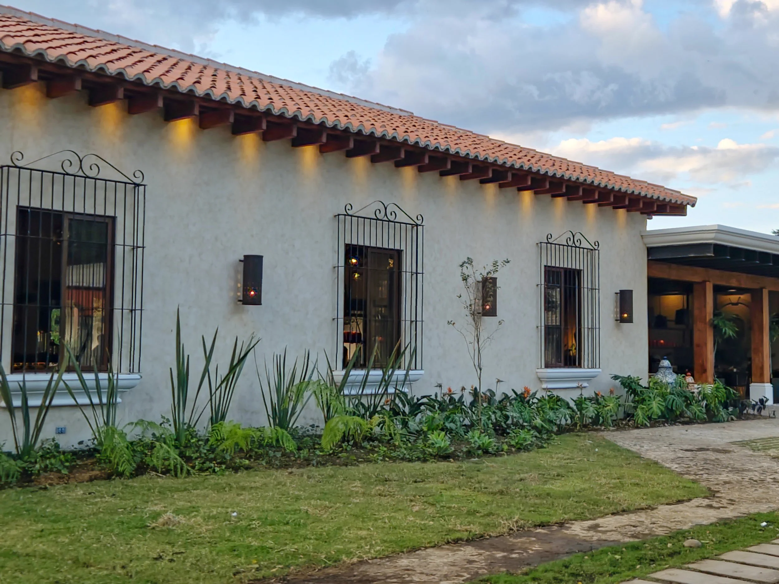 Casa color beige con ventanas protegidas con rejas de hierro, jardineras con plantas y un camino de piedra.