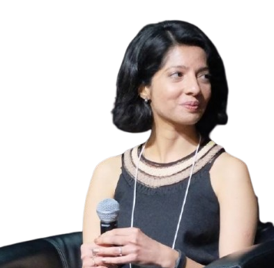 A woman with shoulder-length black hair wearing a sleeveless dress and holding a microphone, sitting against a black background.