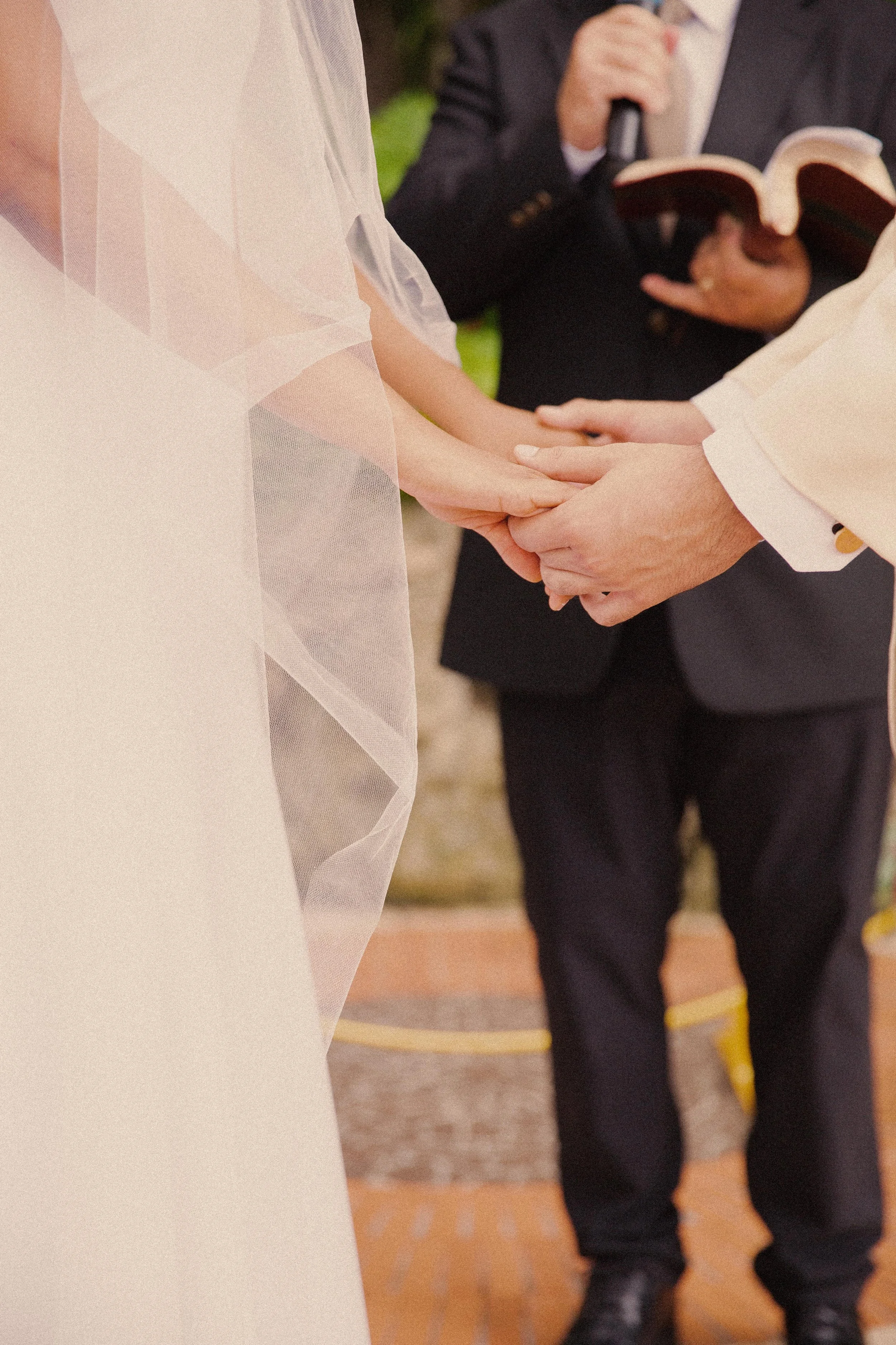Close-up of a wedding ceremony with an officiant holding a microphone and reading from a book, and the bride and groom holding hands.