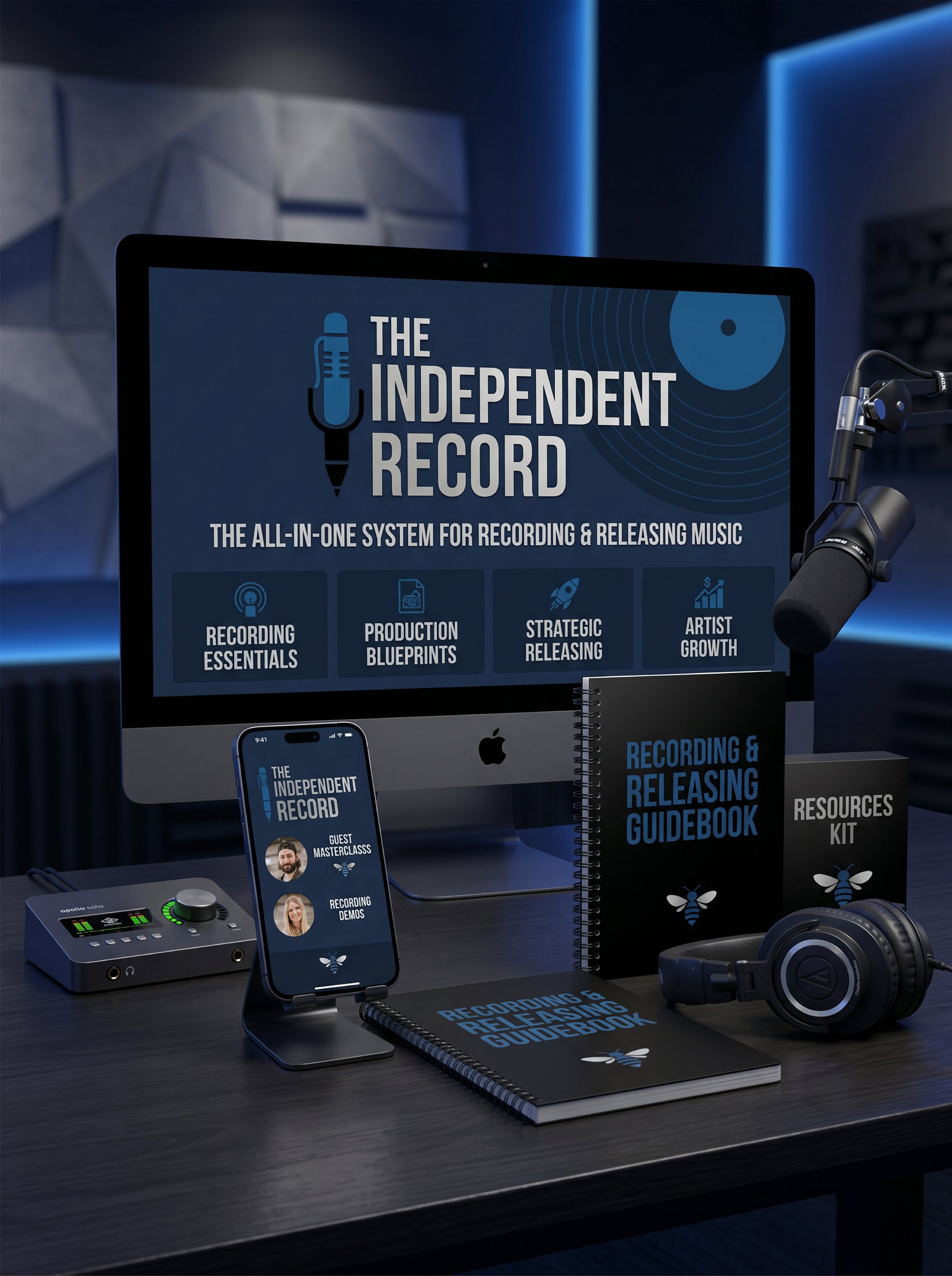 A recording studio workspace featuring a monitor displaying a podcast logo for 'The Independent Record,' a microphone on a boom arm, headphones, a smartphone showing the same logo, a tablet, a notebook titled 'Recording & Releasing Guidebook,' and a kit labeled 'Resources Kit,' all set on a dark wooden desk with acoustic wall panels in the background.