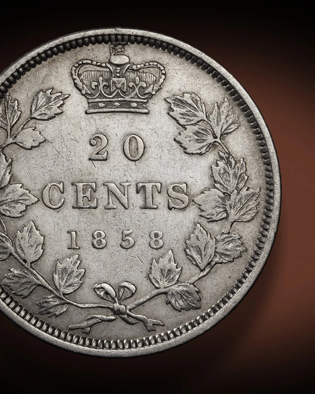 Close-up of a 20-cent coin from 1858, featuring a crown above the denomination and date, surrounded by maple leaves.