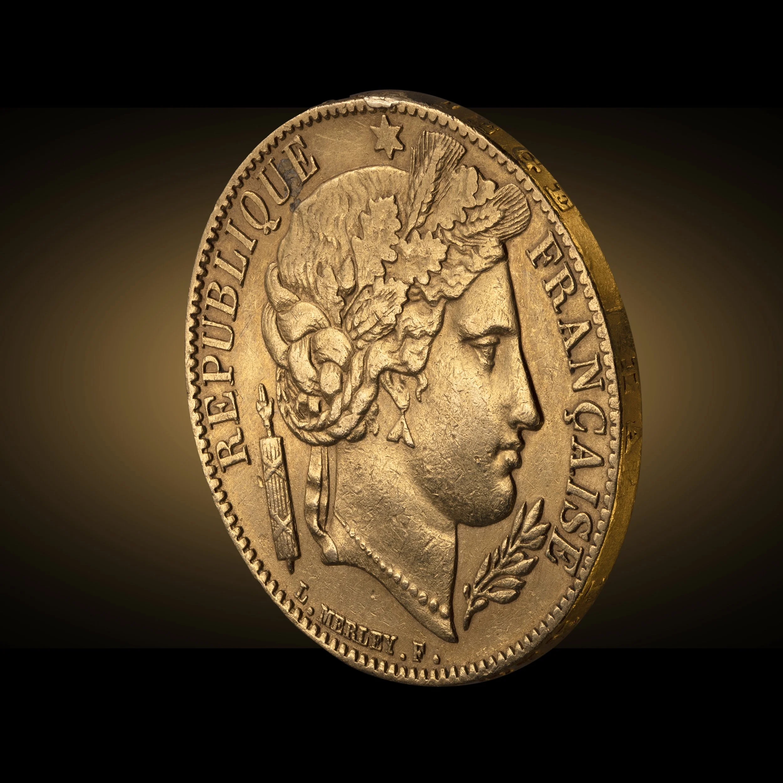 Close-up of a gold coin featuring a profile of a person's face with text around the edge, against a dark background.