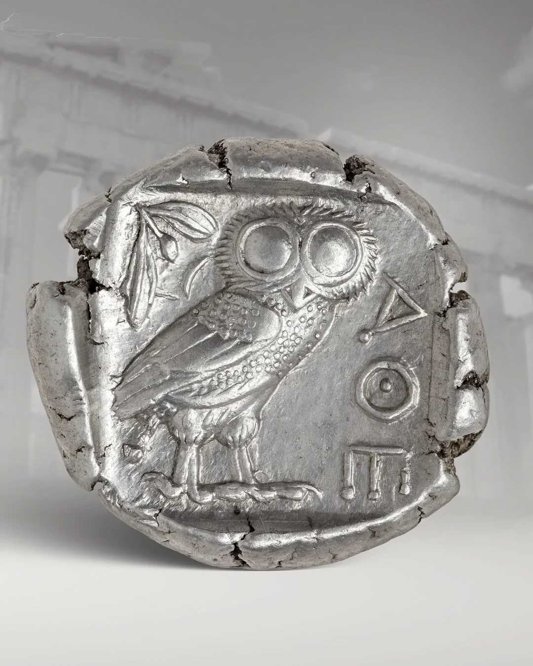 Ancient silver coin featuring an owl wearing large round goggles with an olive branch on the left and various symbols on the right.