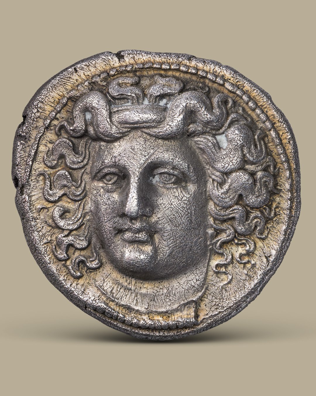 Ancient silver coin with a detailed human face and intricate, curly hair design.