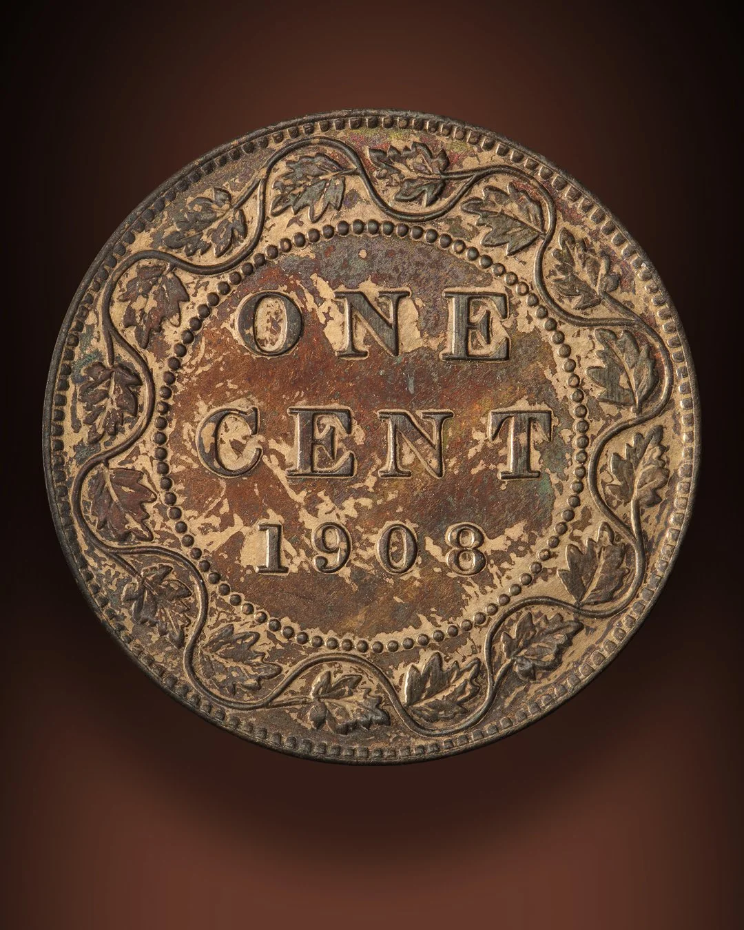 Close-up of a copper coin from 1908 with the words 'ONE CENT' and decorative leaf patterns around the edge.