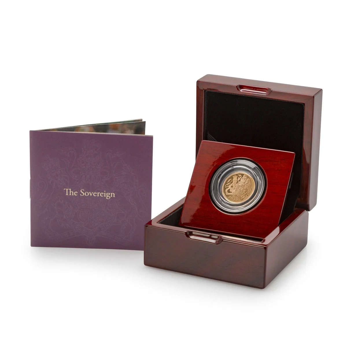 A gold coin with a lion emblem inside a clear protective case, placed in a polished wooden display box, with a purple booklet titled 'The Sovereign' next to it.