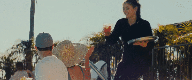 A server brings drinks to people at an outdoor setting with palm trees.