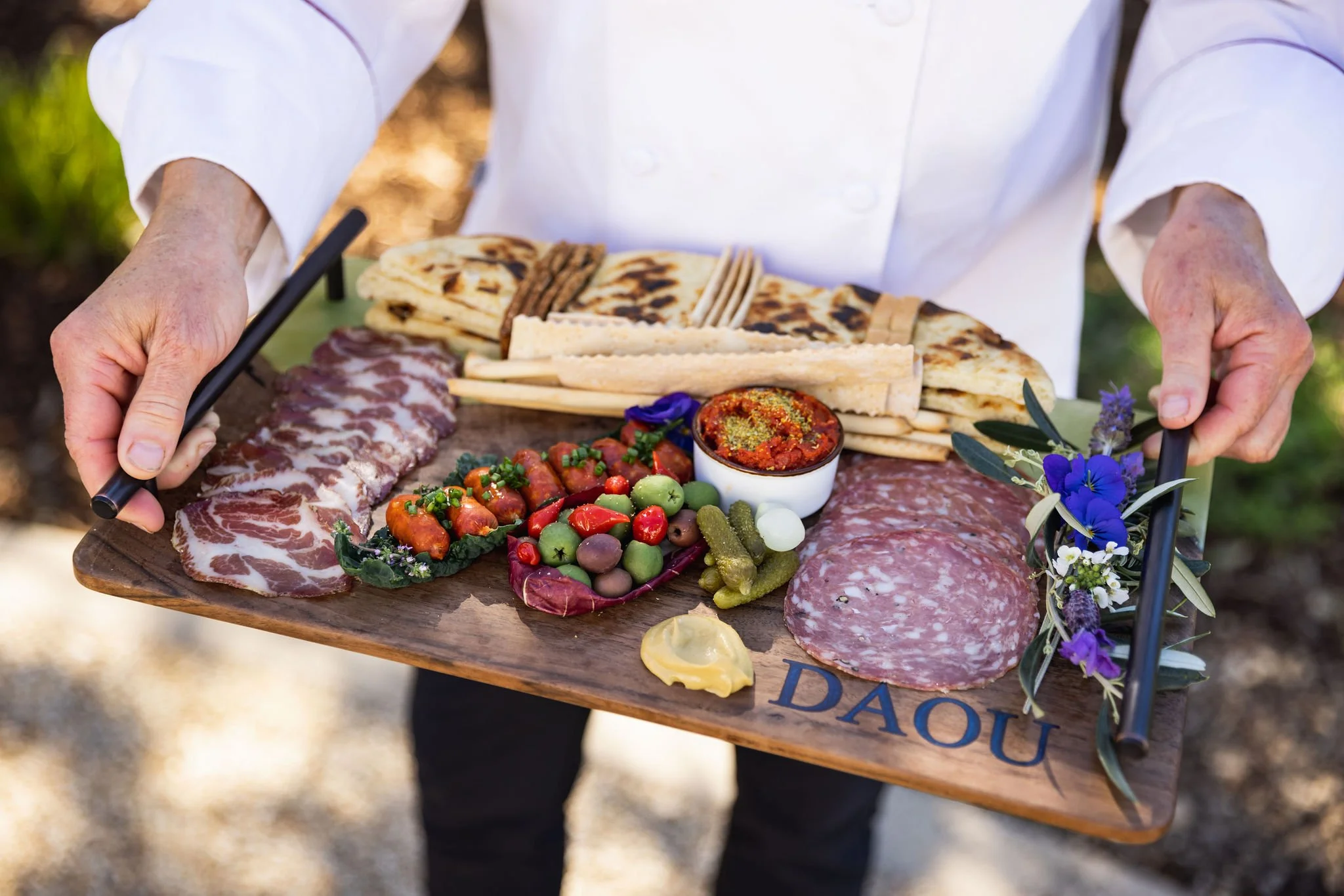 Charcuterie board with cured meats, olives, crackers, dip, and garnishes.