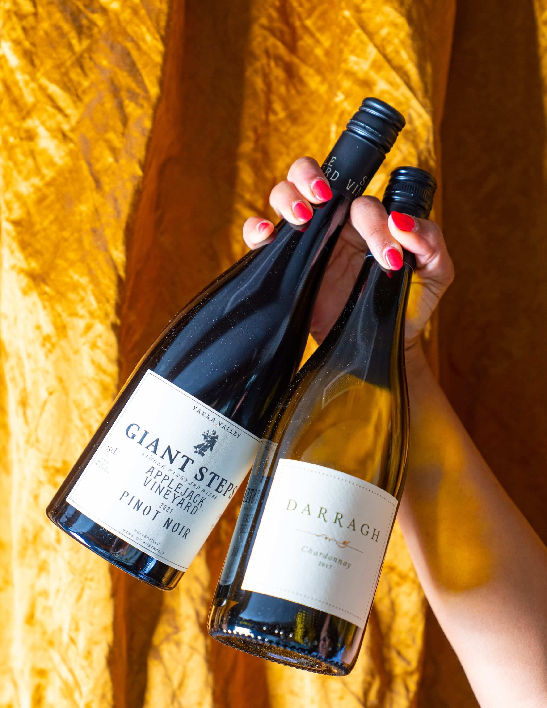  A hand holding up a bottle of Chardonnay and Pinot Noir against a gold background 