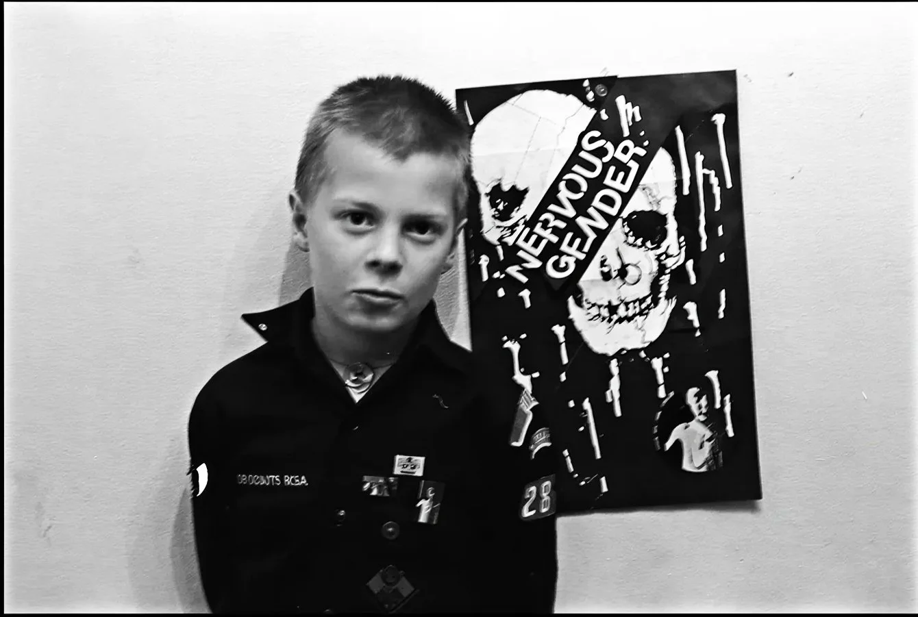 Sven Pfeiffer standing in front of a Nervous Gender Reloaded poster connected to the Los Angeles synthpunk and industrial music underground