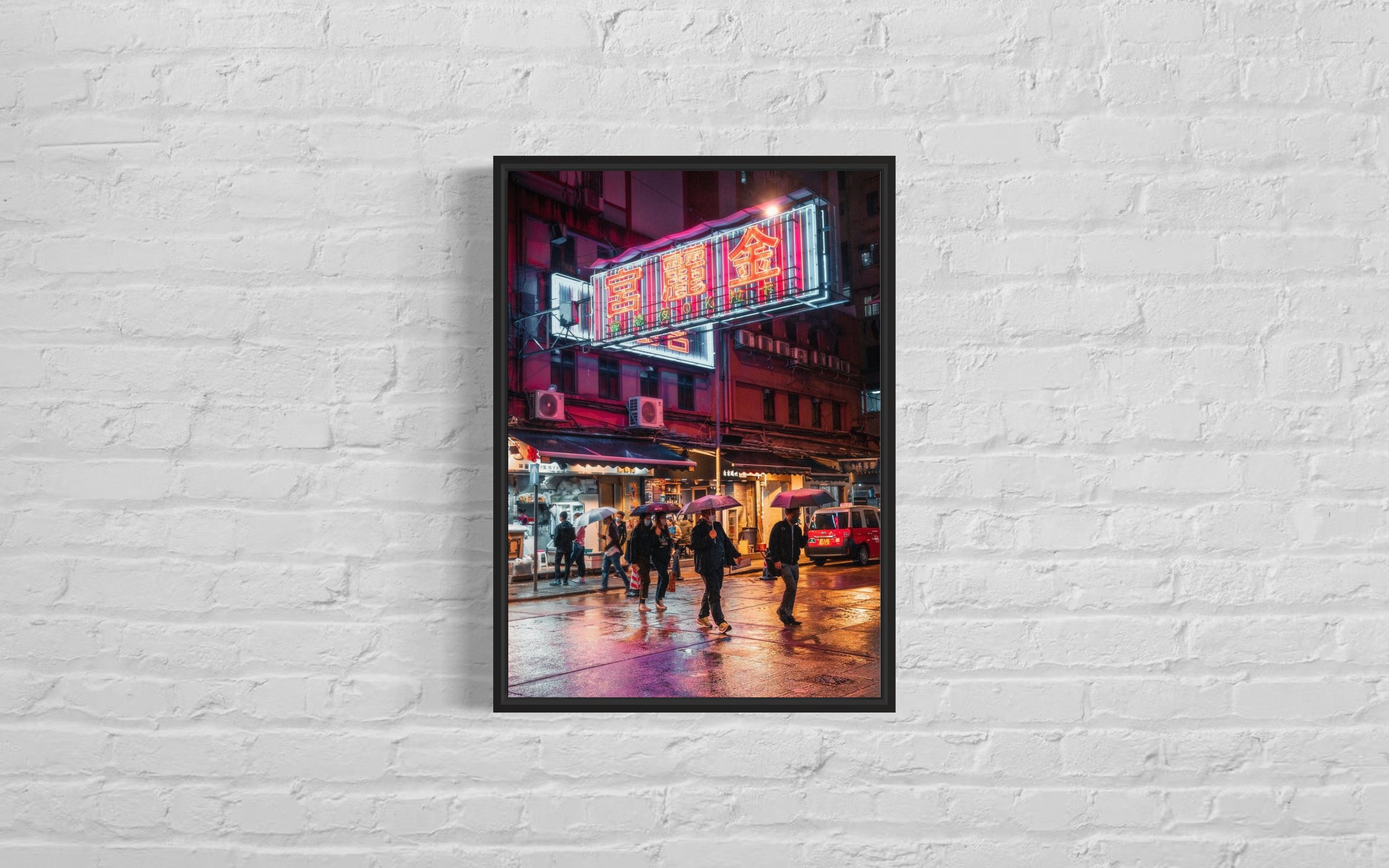 Framed photographic image of people holding umbrellas walking under a neon sign in Mongkok, Hong Kong.