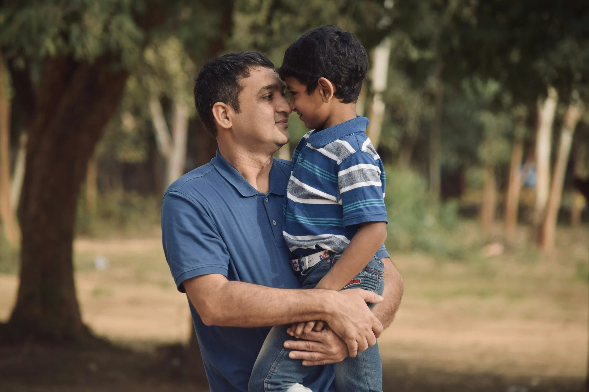 A father holding his young son close, foreheads touching, in a park — a moment of calm connection between parent and child.