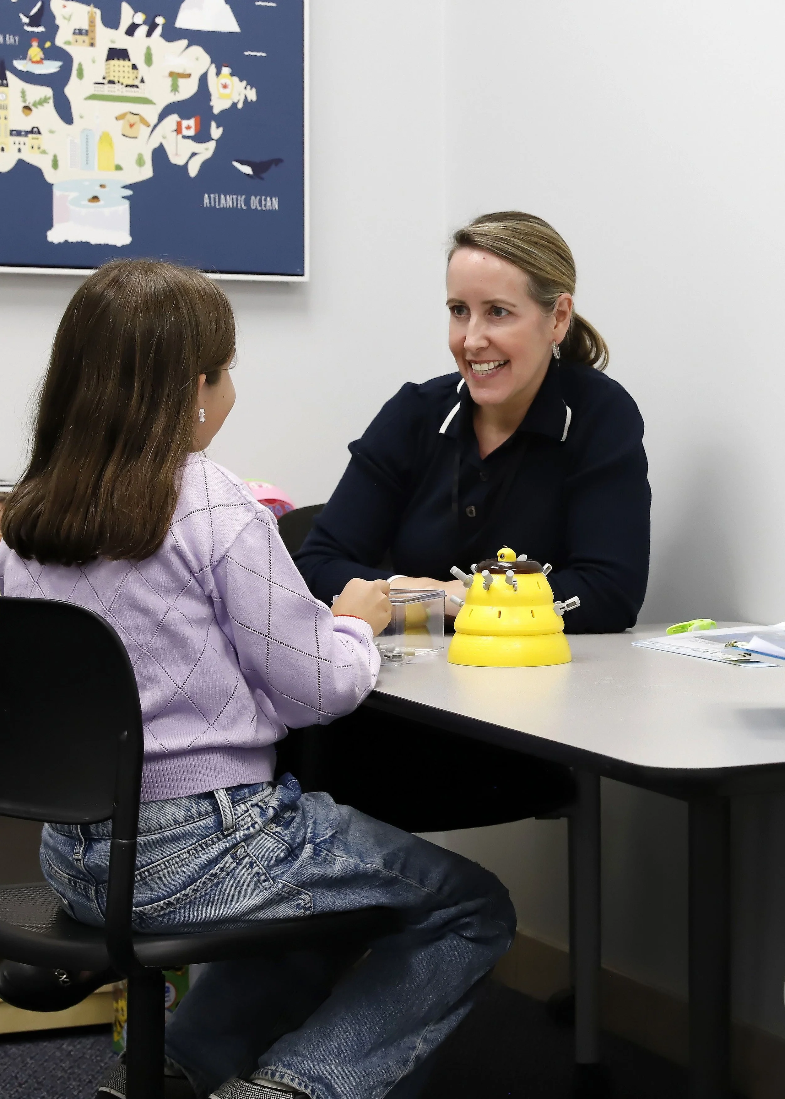 A behaviour analyst working one-on-one with a child at a therapy table, engaged in a structured activity in a bright clinical setting