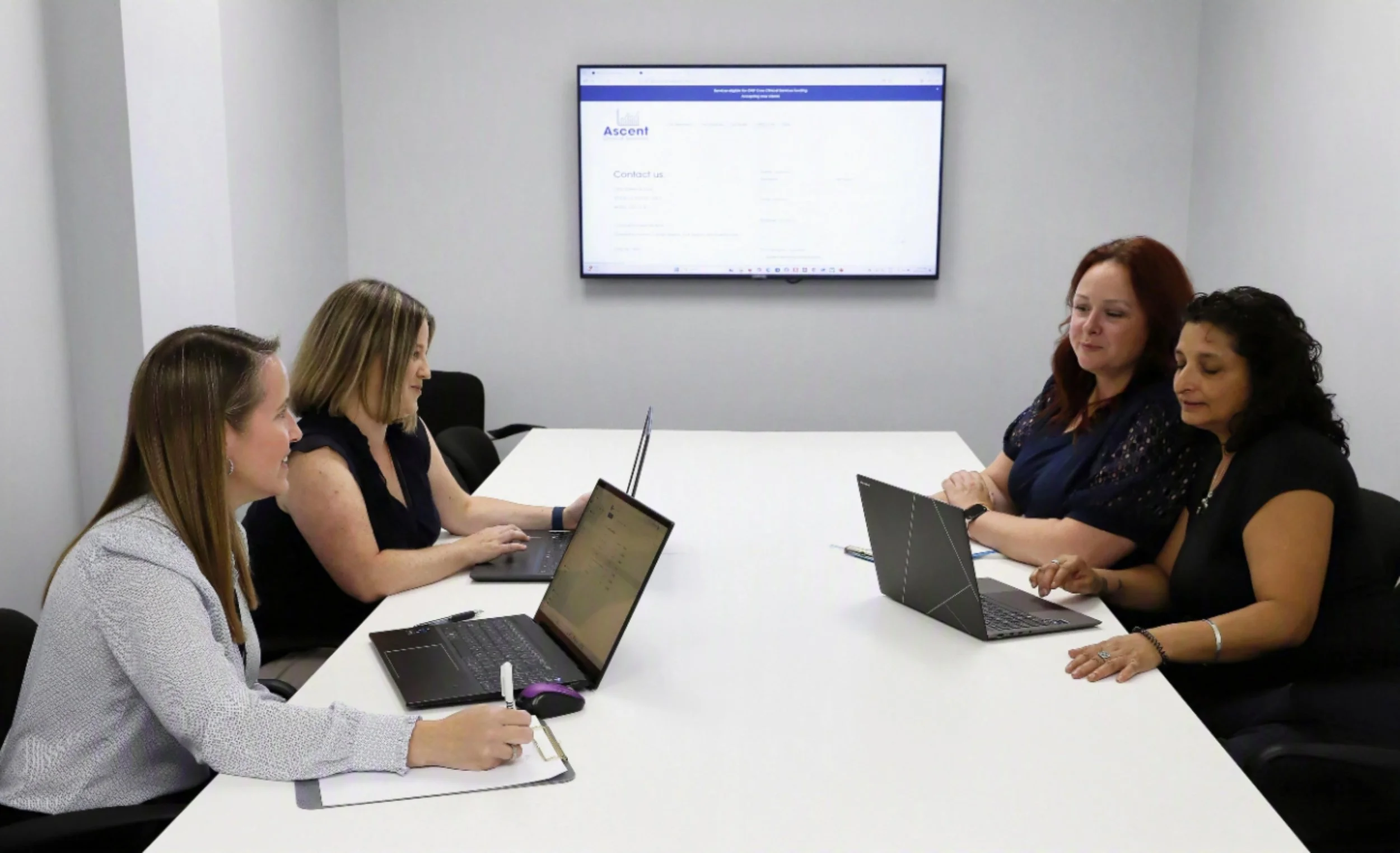 The Ascent Clinical Services team collaborating in a meeting room, reviewing client information on laptops as part of their interprofessional approach to care.