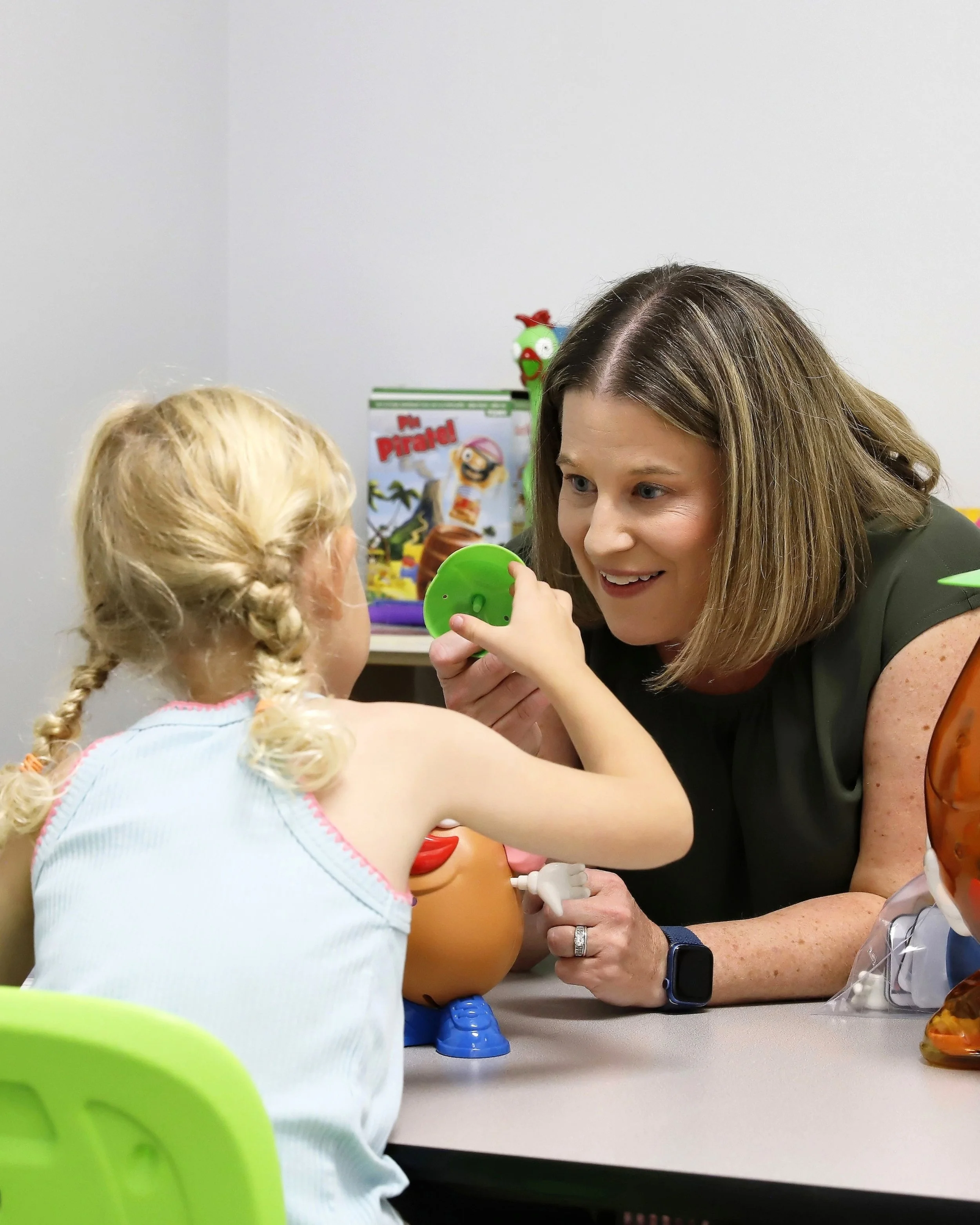A behaviour analyst engaging a young child in a play-based therapy activity, using toys to support learning and skill development in a clinical setting
