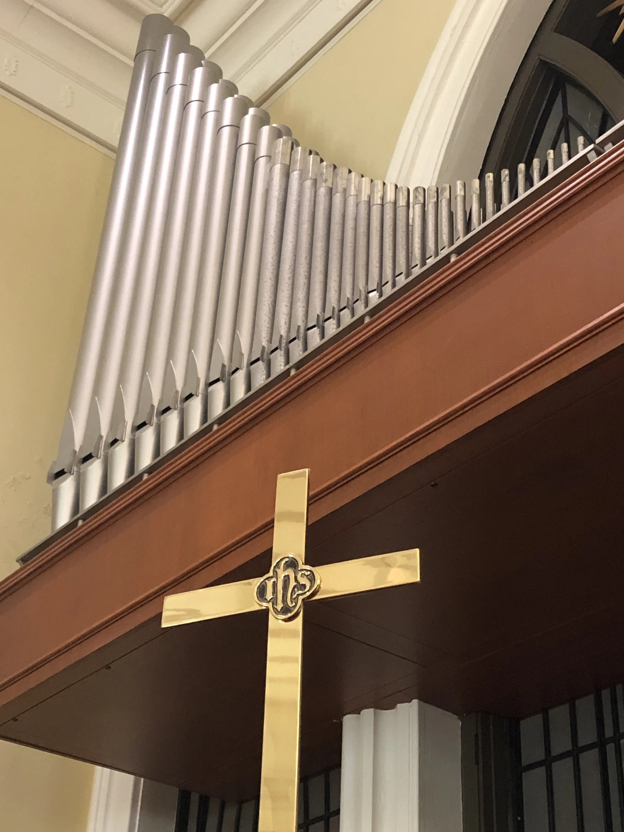Close-up of a church or chapel organ pipes and a wooden altar with a gold-colored cross.