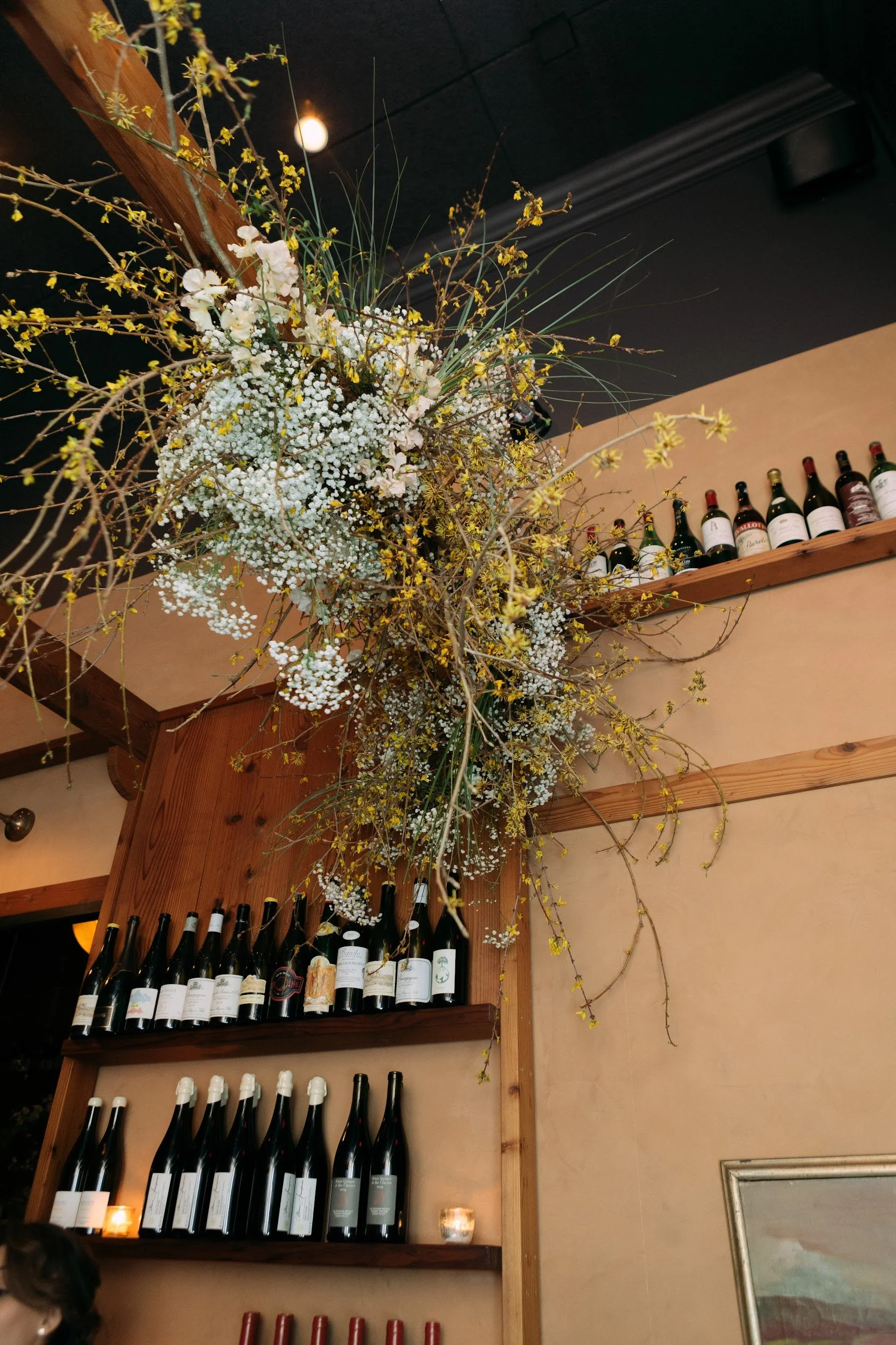 Hanging floral installation above wine shelves at a Los Angeles restaurant wedding reception.