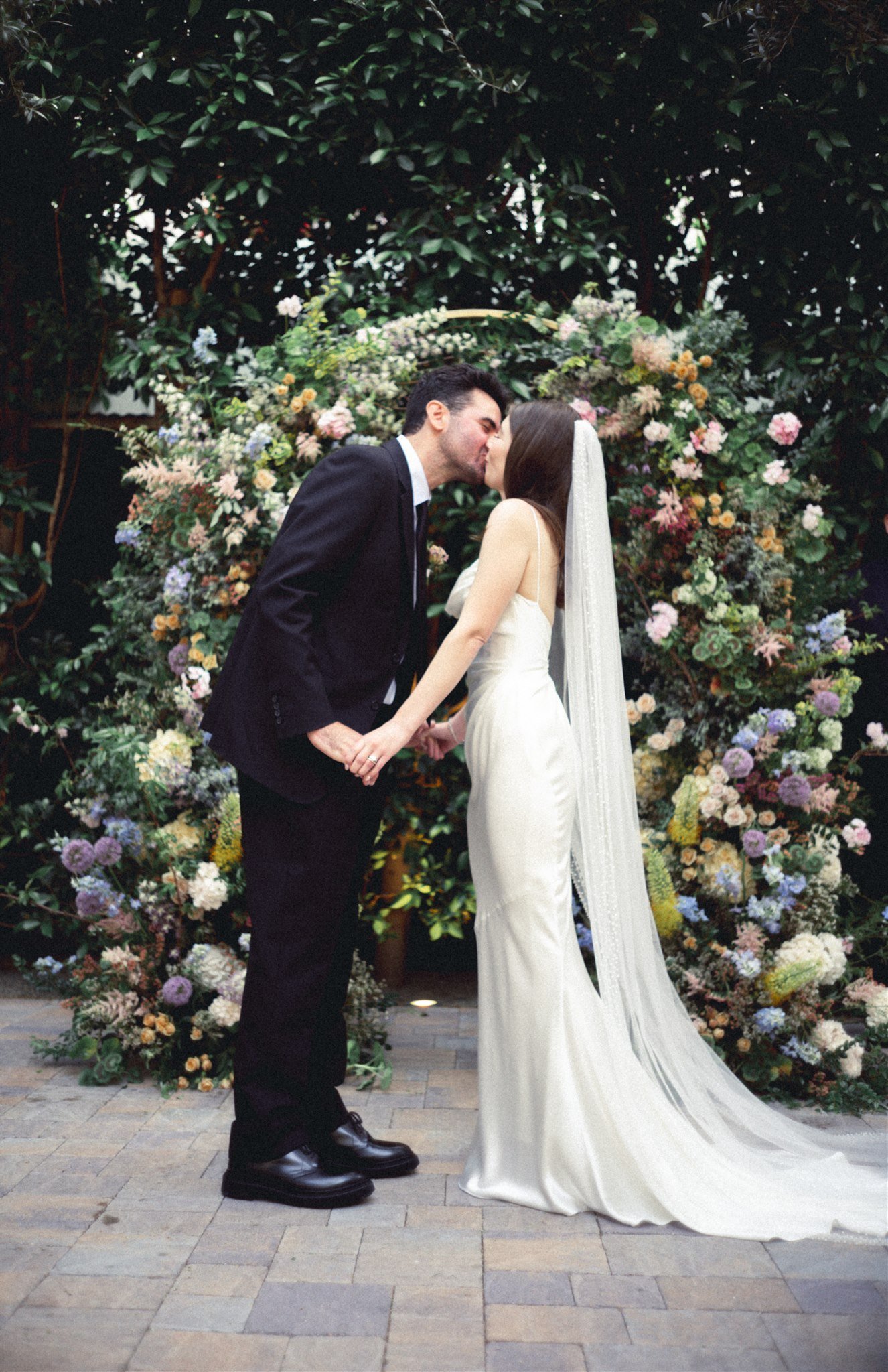 Bride and groom sharing a kiss beneath a floral arch at a Southern California ceremony designed by Moon Realm.
