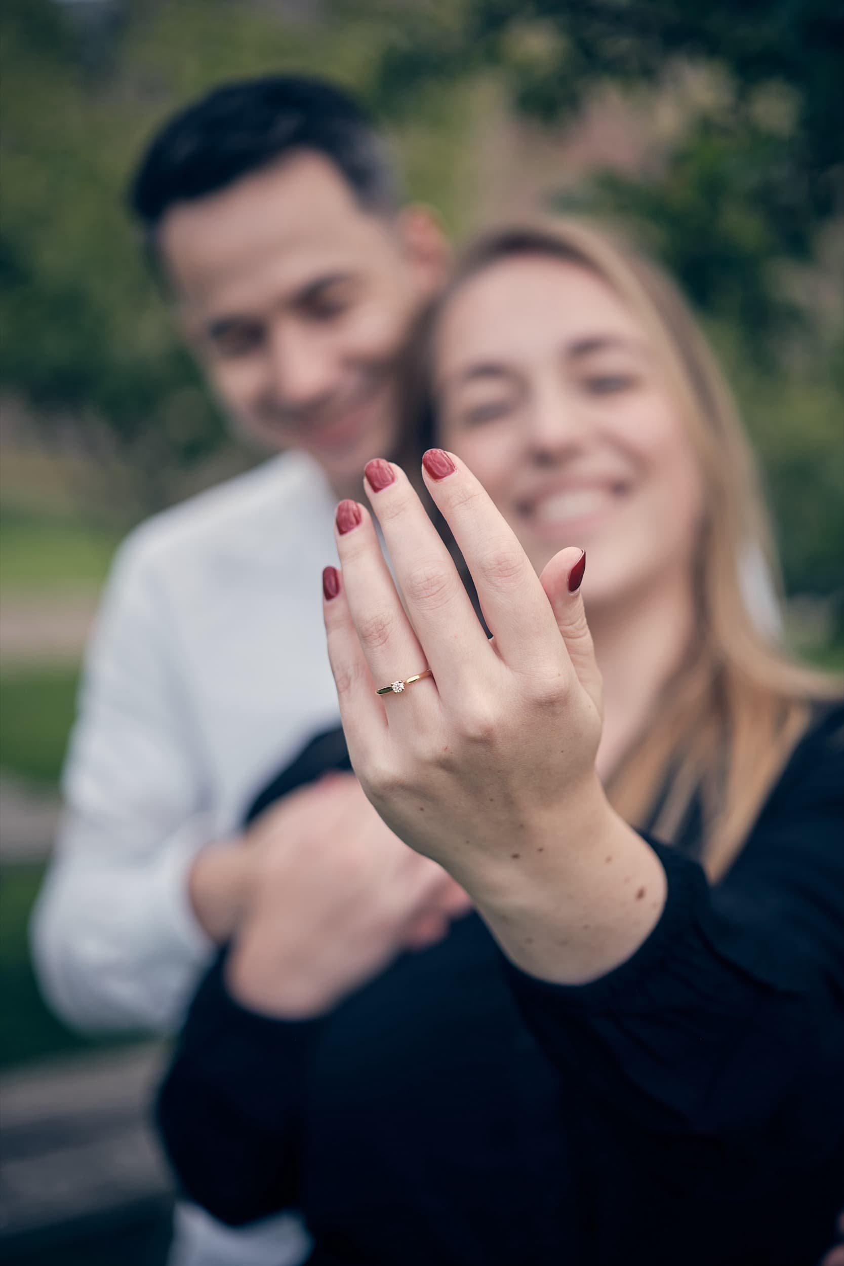 Vrolijk stel toont verlovingsring op hun hand met lach op hun gezicht, op de achtergrond een groene omgeving.