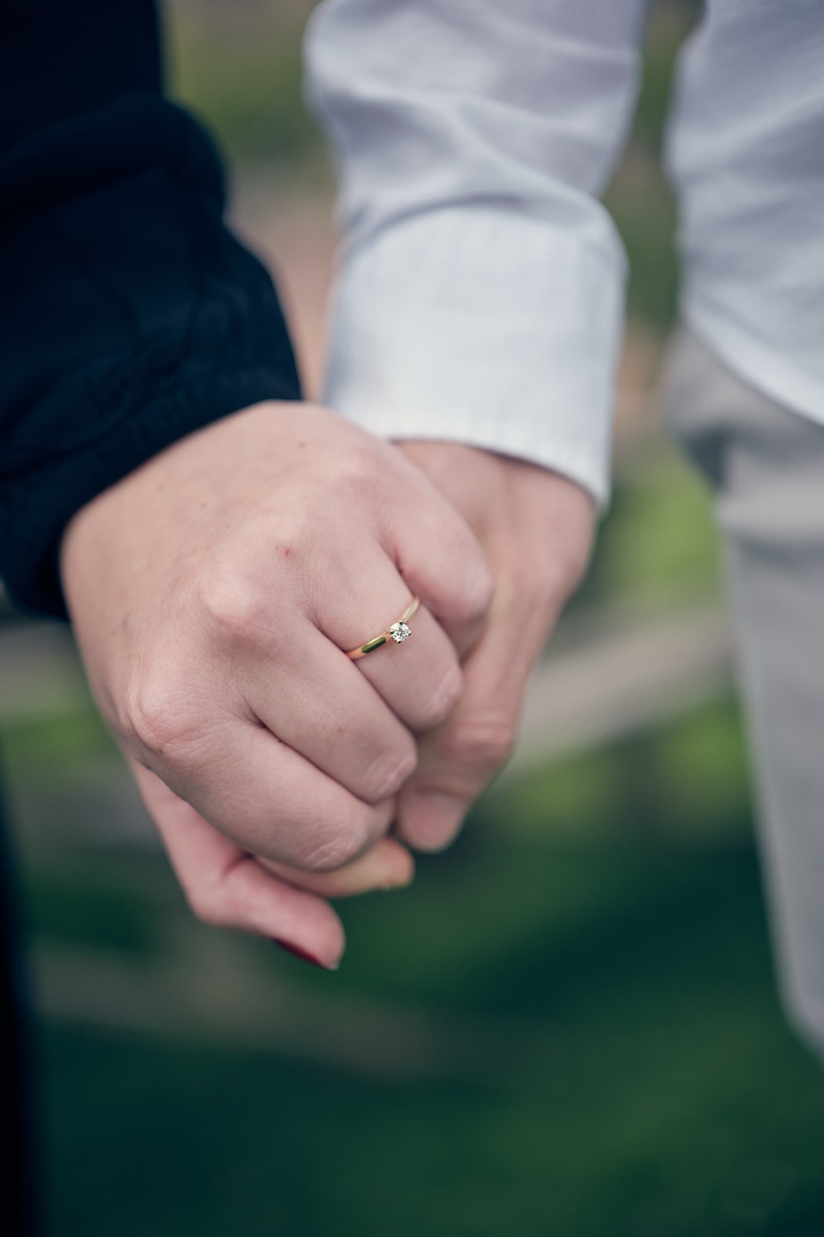Close-up van twee mensen die elkaars handen vasthouden, met een ring op de vinger van één persoon.