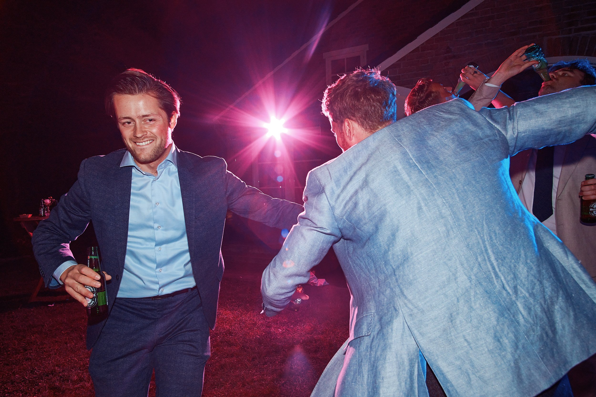 Mannen dansen en drinken op een feestje, met kleurrijk licht en een feestelijke sfeer.