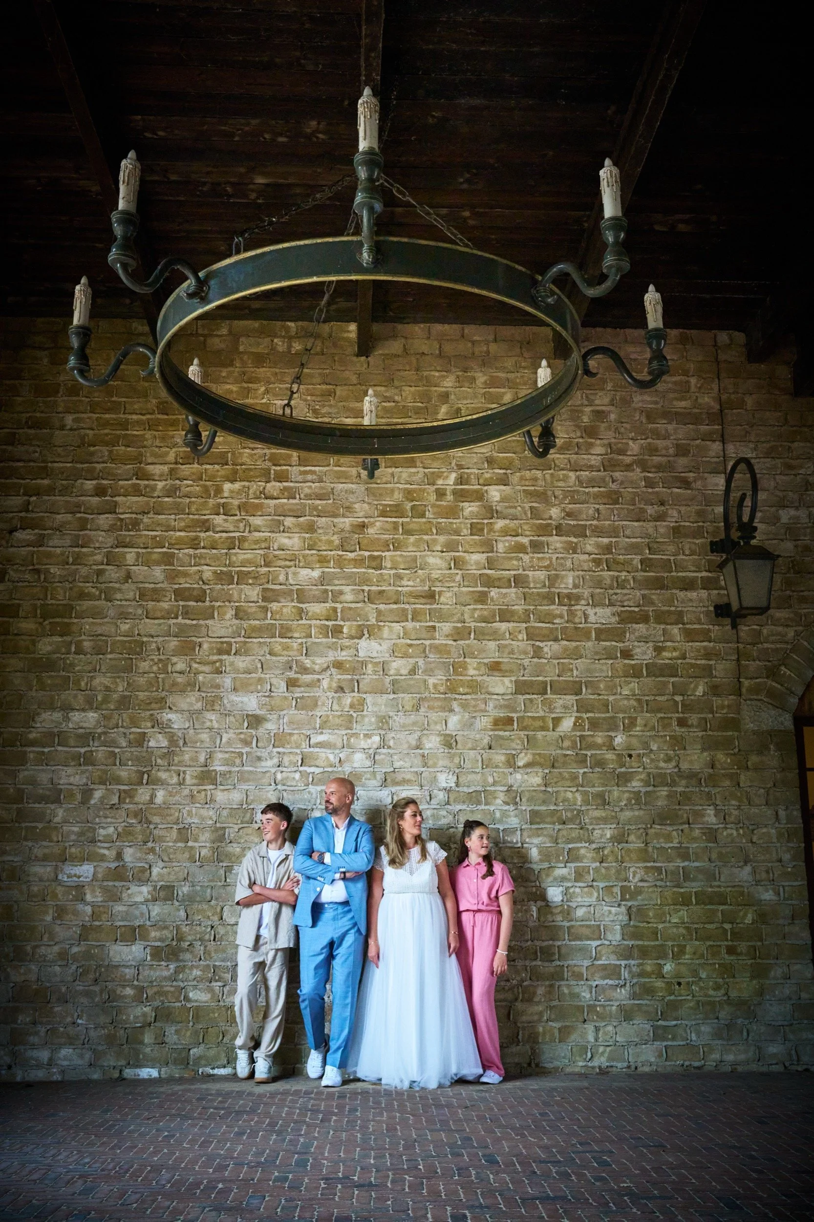 Vier mensen staan samen in een ruimte met een bakstenen muur en hanglamp. Ze lijken te poseren voor een foto.