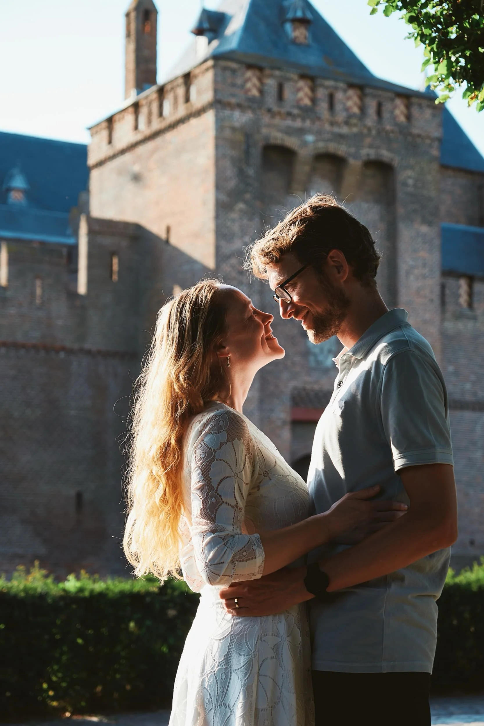Een stel dat elkaar liefdevol aankijkt voor een oud kasteel op de achtergrond.