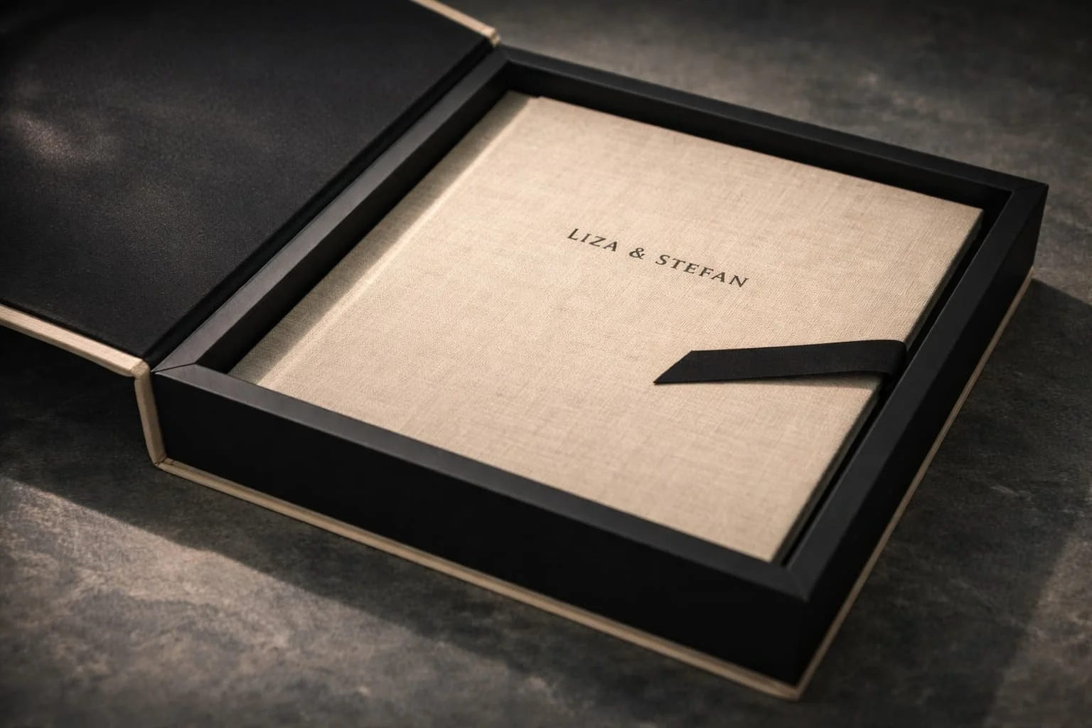 Geschenkdoos met een beige boekje met de tekst 'LIZA & STEFAN' erop, in een zwarte doos met een zwarte lint.