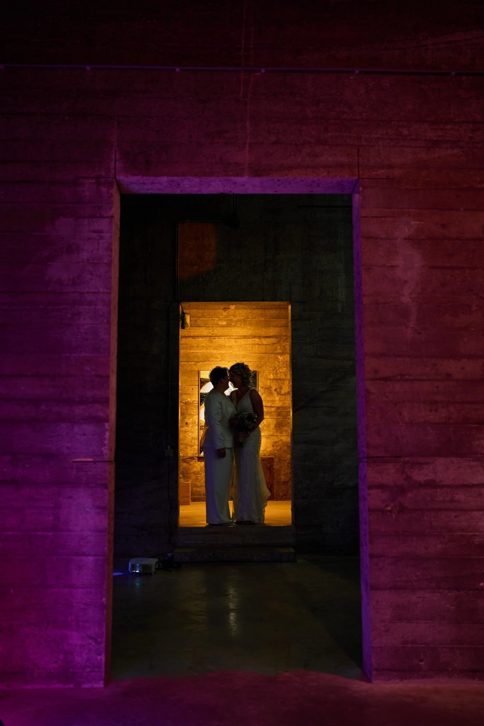 Twee mensen die intiem naar elkaar kijken, in een warme, houten ruimte, onder zacht oranje en paarse verlichting.