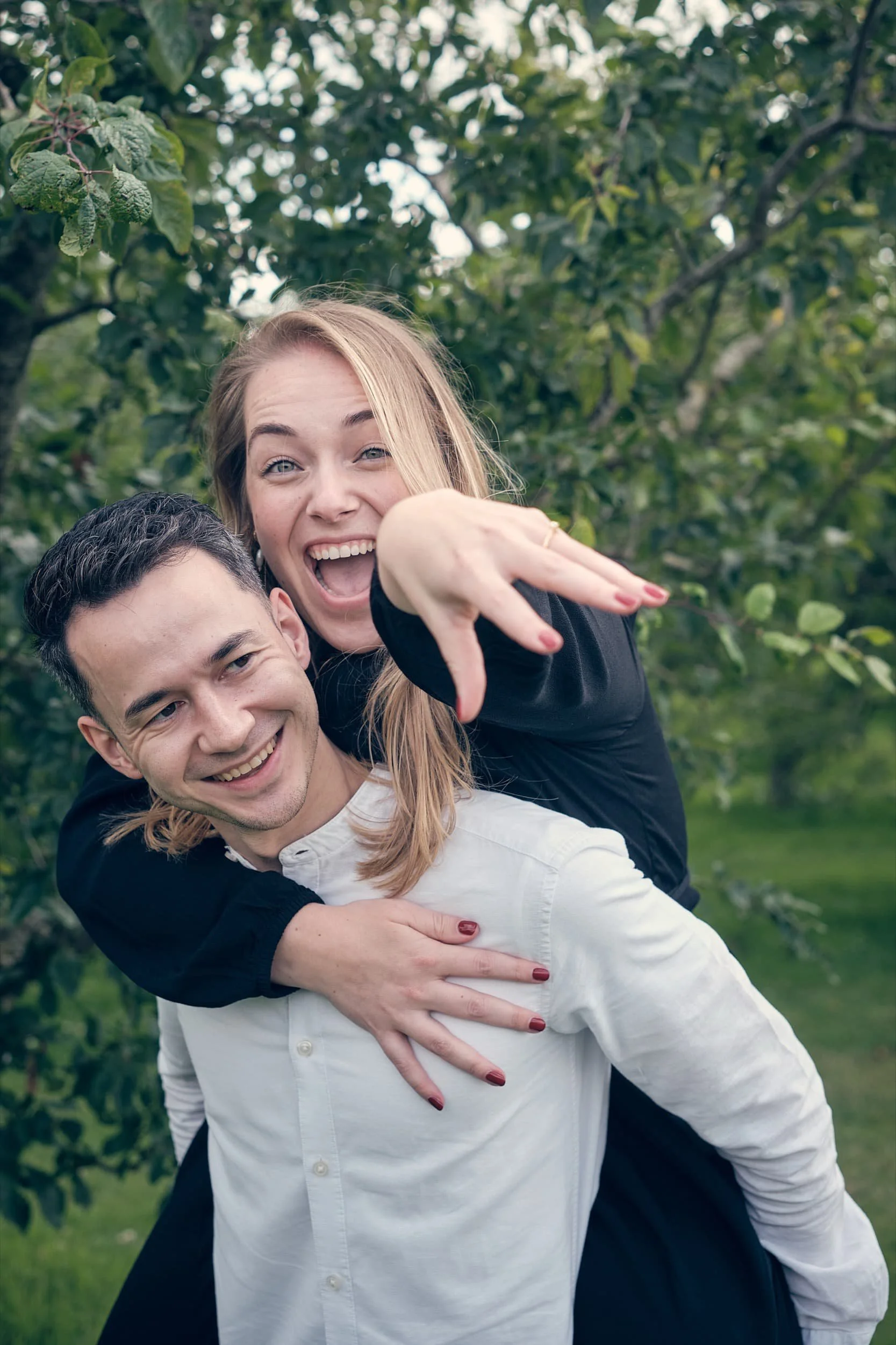 Twee lachende mensen, een man en een vrouw, plezierig in een groene tuin, de vrouw op de rug van de man en wijst naar de camera.