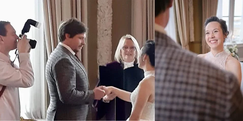 Een bruiloftsceremonie waarbij een bruid en bruidegom elkaar de hand schudden tijdens de ondertekening van een document, terwijl een fotograaf foto's maakt en een trouwambtenaar toekijkt.