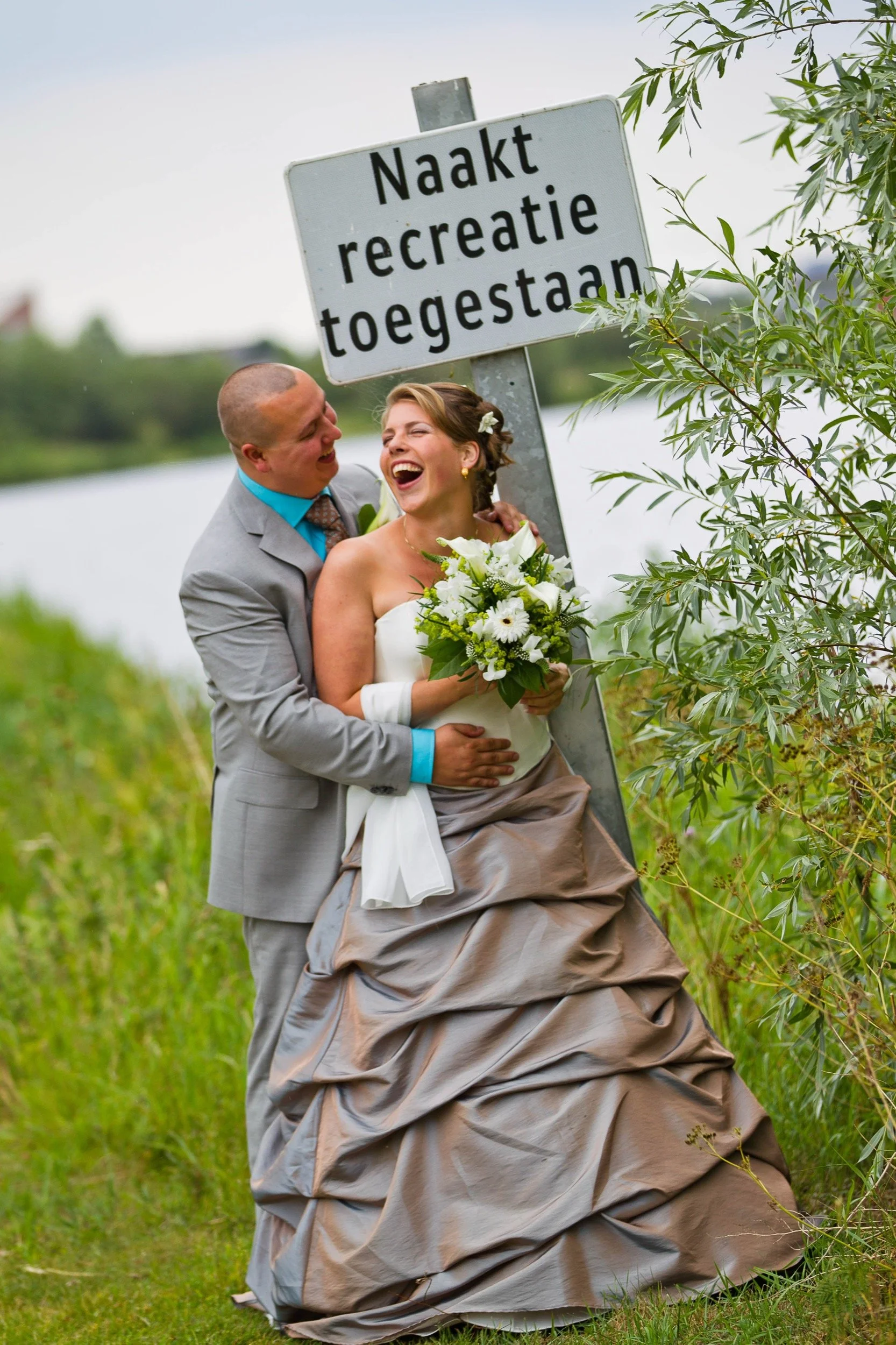 Een huwelijkspaar naast een bord dat zegt dat naakt recreatie is toegestaan, lachend en in een gelukkige bui.