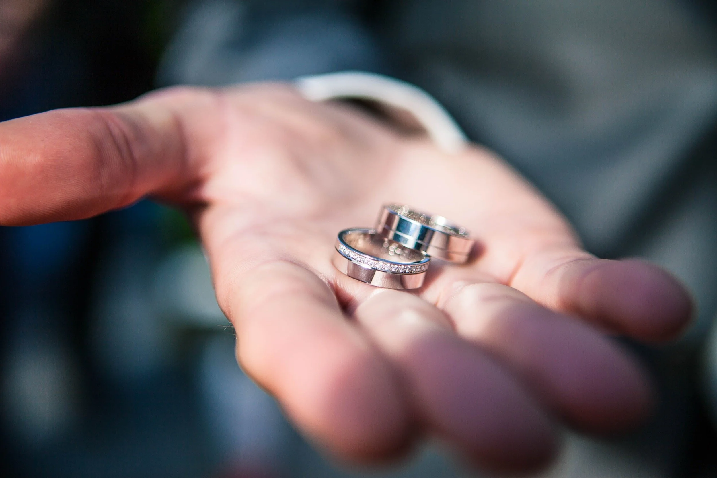 Een hand houdt drie ringen, waaronder een met kleine diamanten, terwijl de achtergrond onduidelijk is.