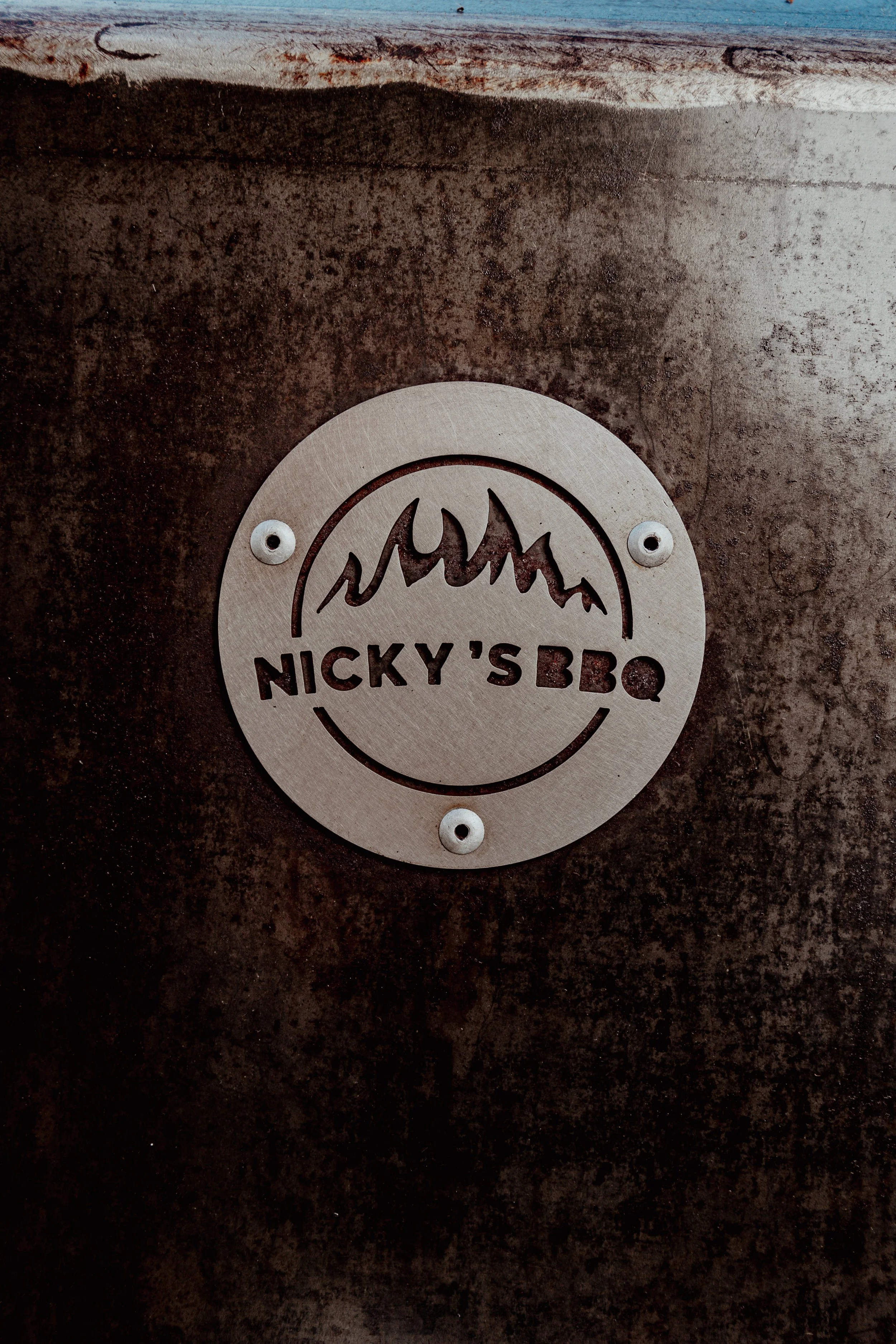 Plaque en métal indiquant "Nicky's BBQ" avec un dessin de montagnes stylisées.
Food truck reims. location de braséro. Evenements, traiteur. fabricant de barbecues made in france.
