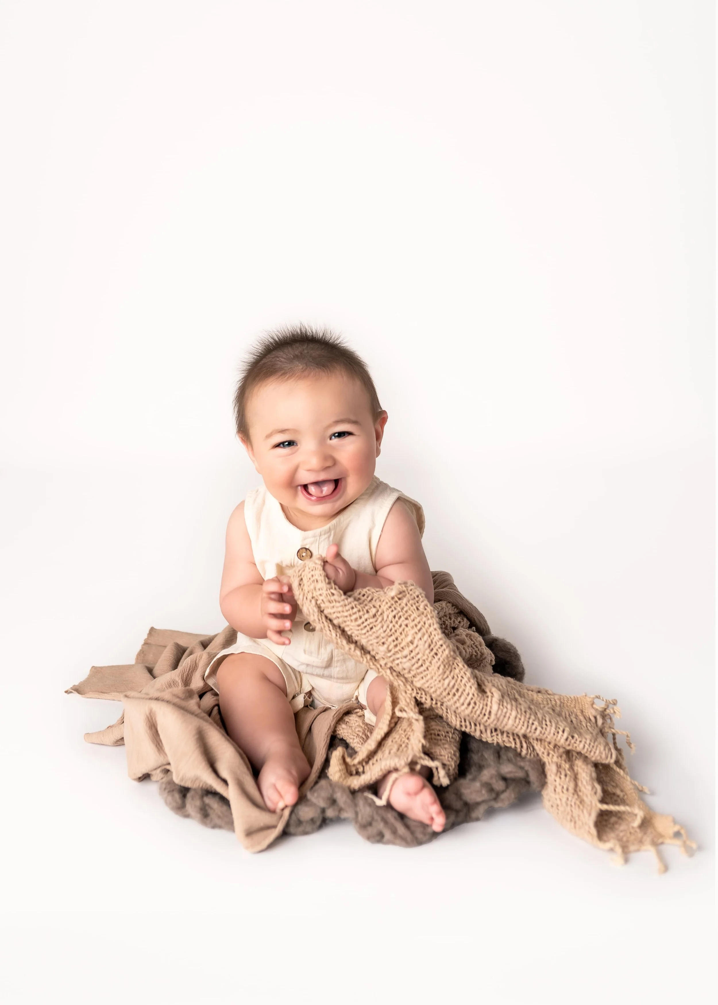 image of baby boy sitting on brown layers laughing for his half birthday milestone photoshoot in a photography studio in Canton, GA