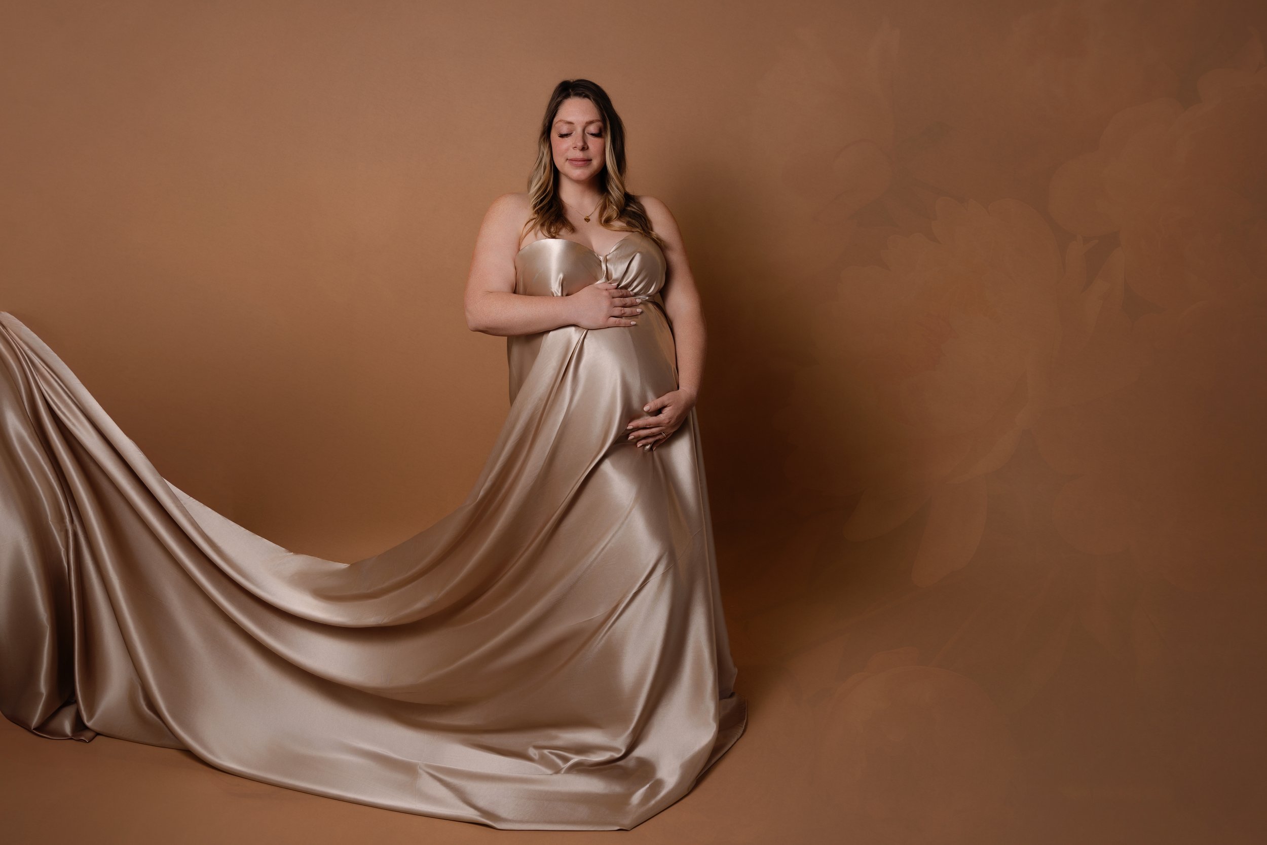 pregnant mom to be in photography studio posed on neutral background with gold fabric