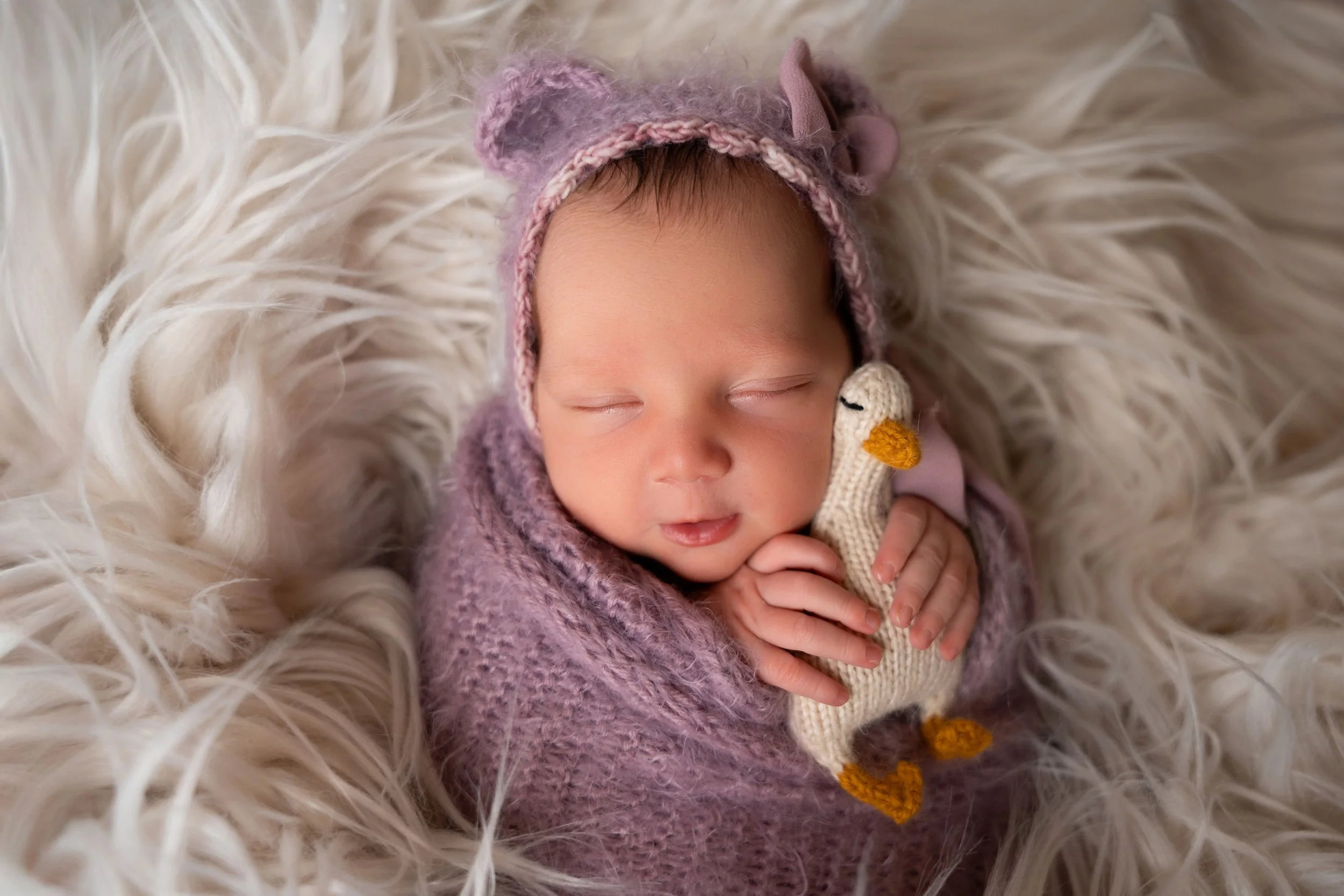 image of newborn baby swaddled and posed on fur with bonnet smiling for camera in photography studio in Canton GA