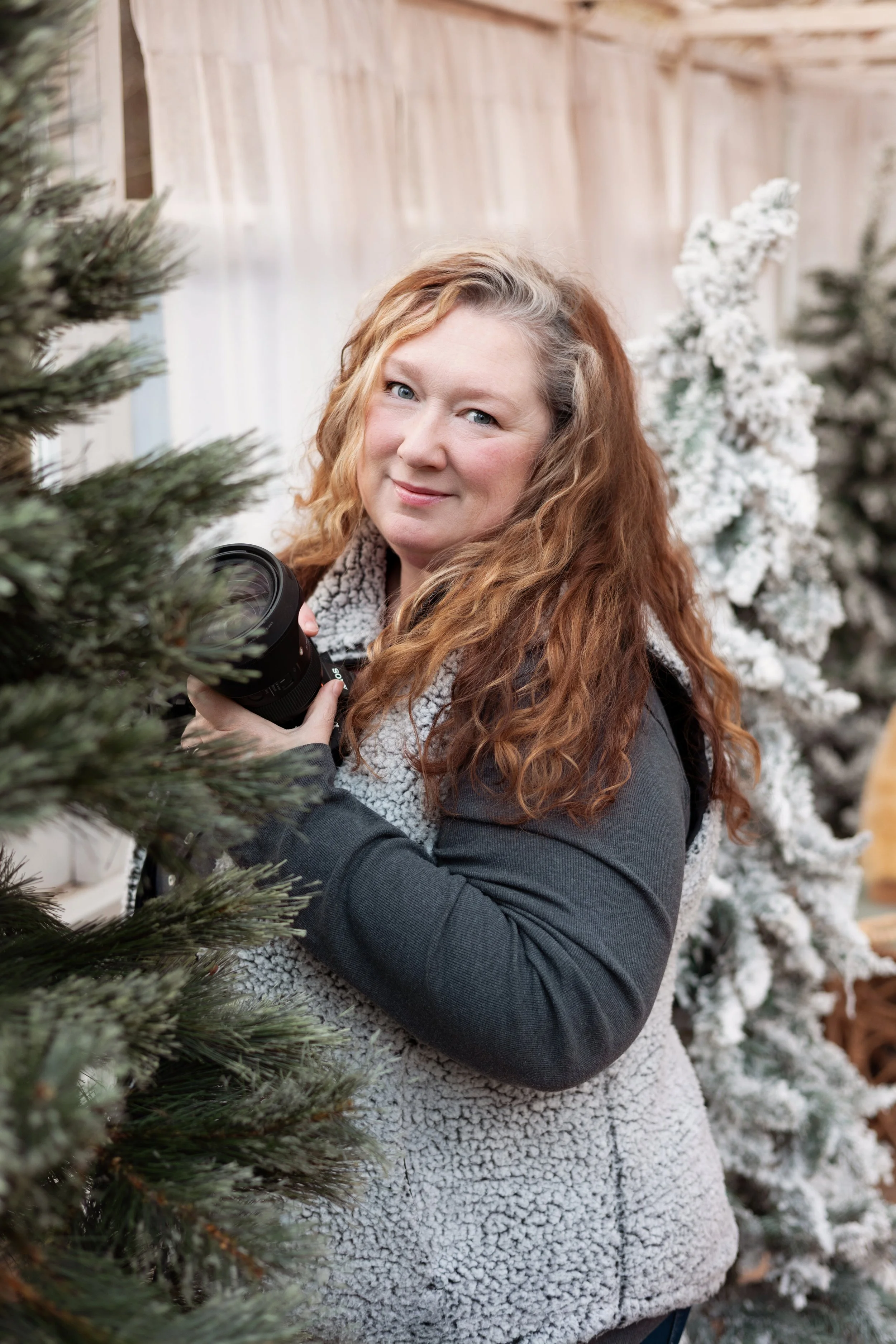 image of Cindy holding her camera in a greenhouse setting with Christmas trees
