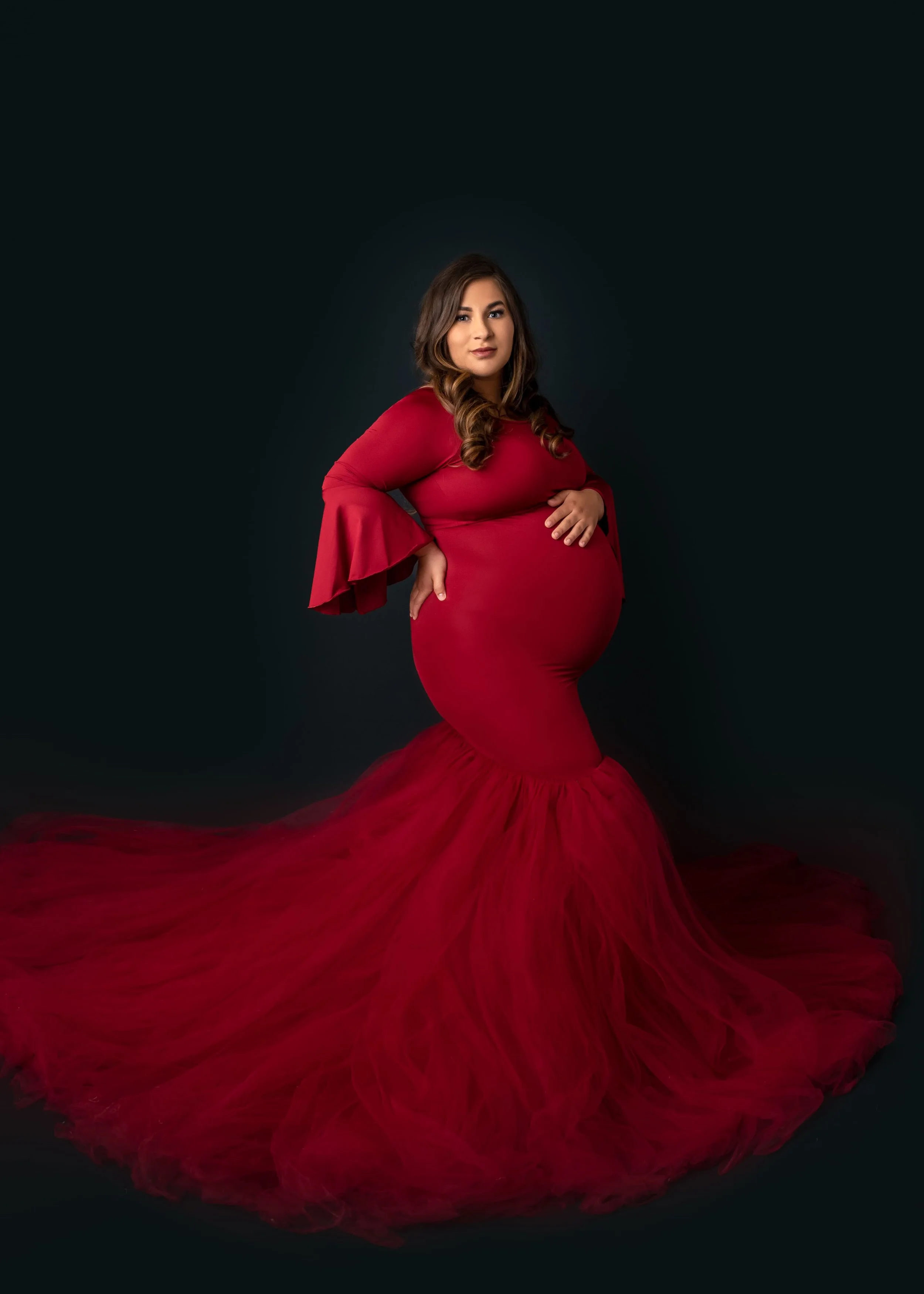 studio maternity portrait of expectant mother in a bold red gown highlighting her pregnant belly in Ball Ground, GA