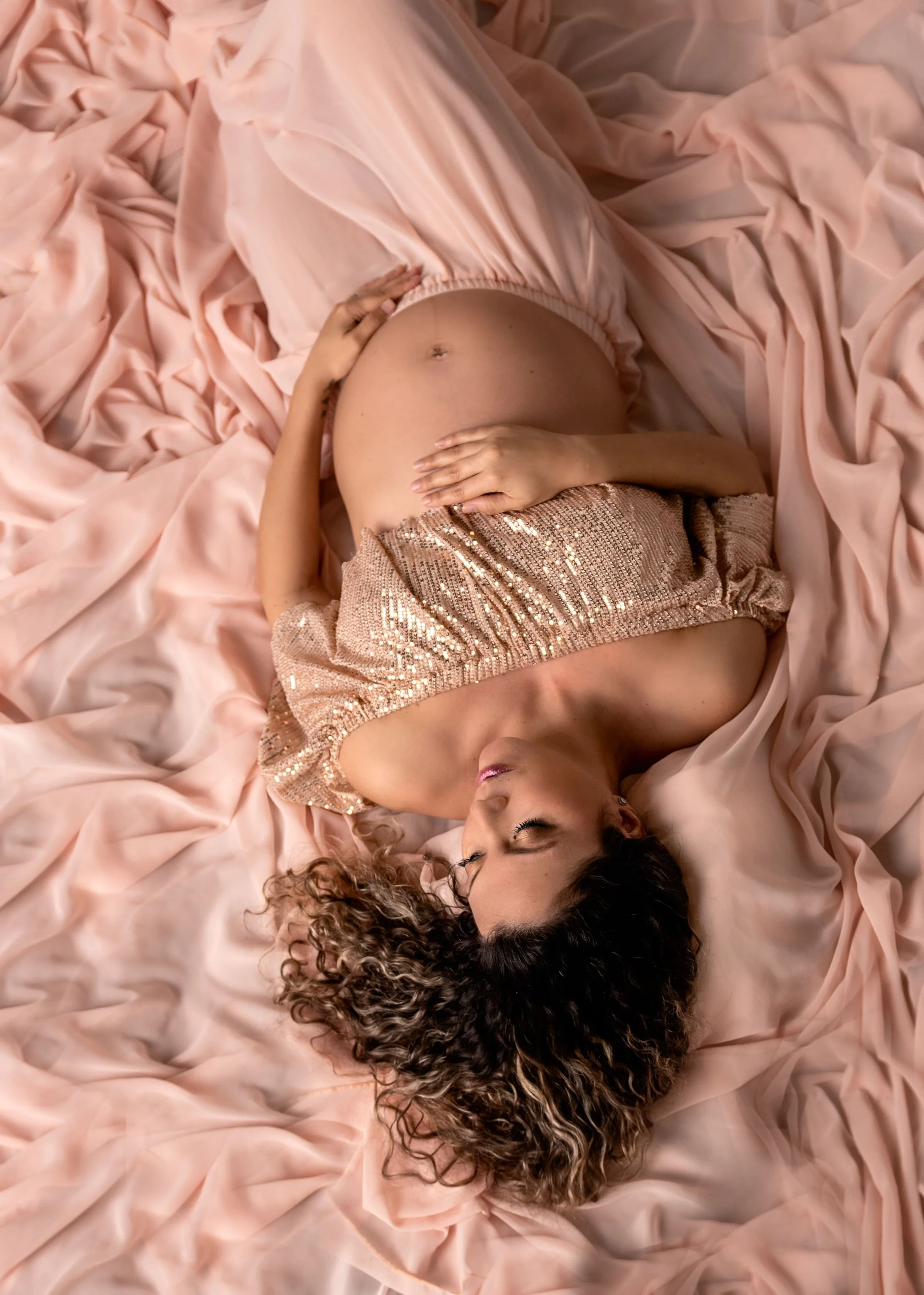 studio maternity portrait of expectant mother laying down on a soft pink gown revealing her pregnant belly in Woodstock GA