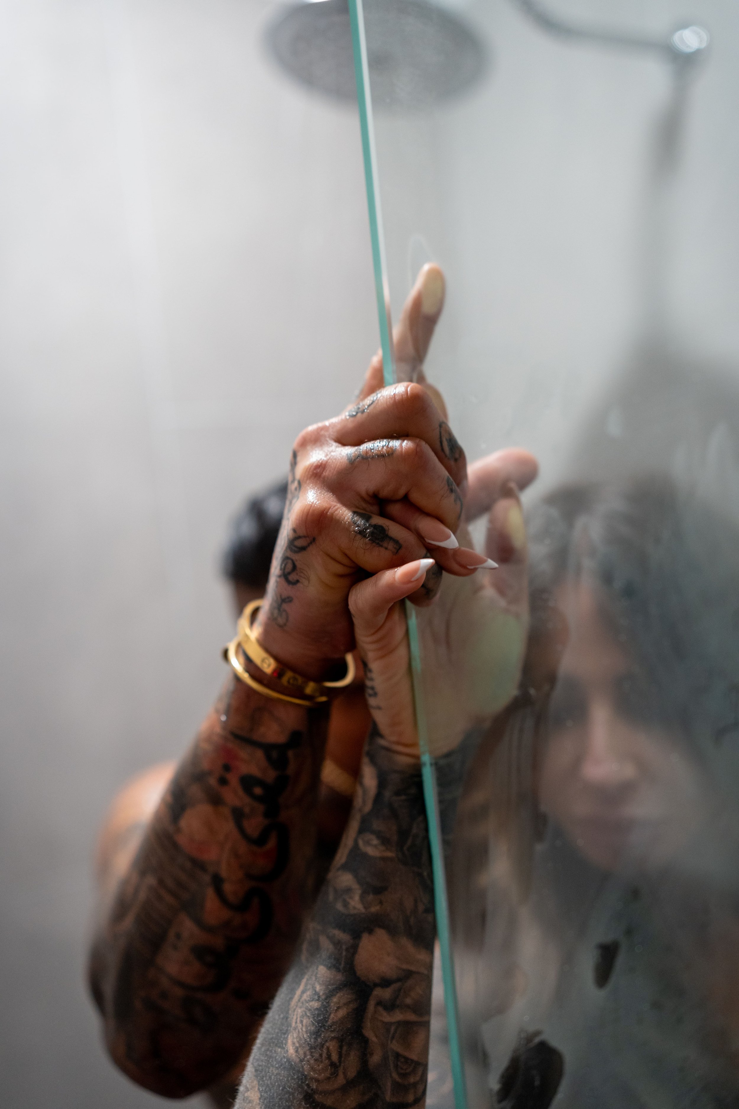 Person with multiple tattoos touching a glass surface, with their face reflected in the glass