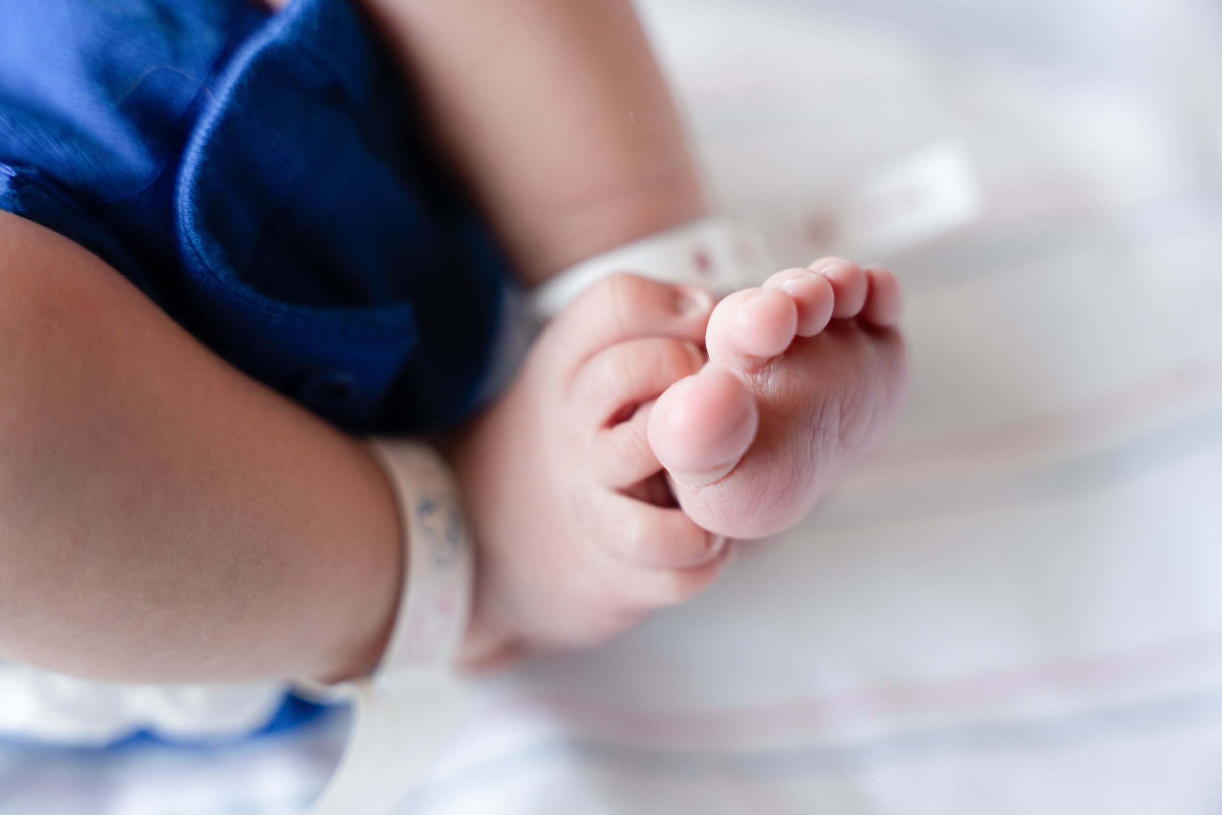 newborn photographer taking Fresh48 picture of baby in Cumming GA hospital closeup of baby feet of a baby born just 24 hours prior in the hospital with ankle bands on