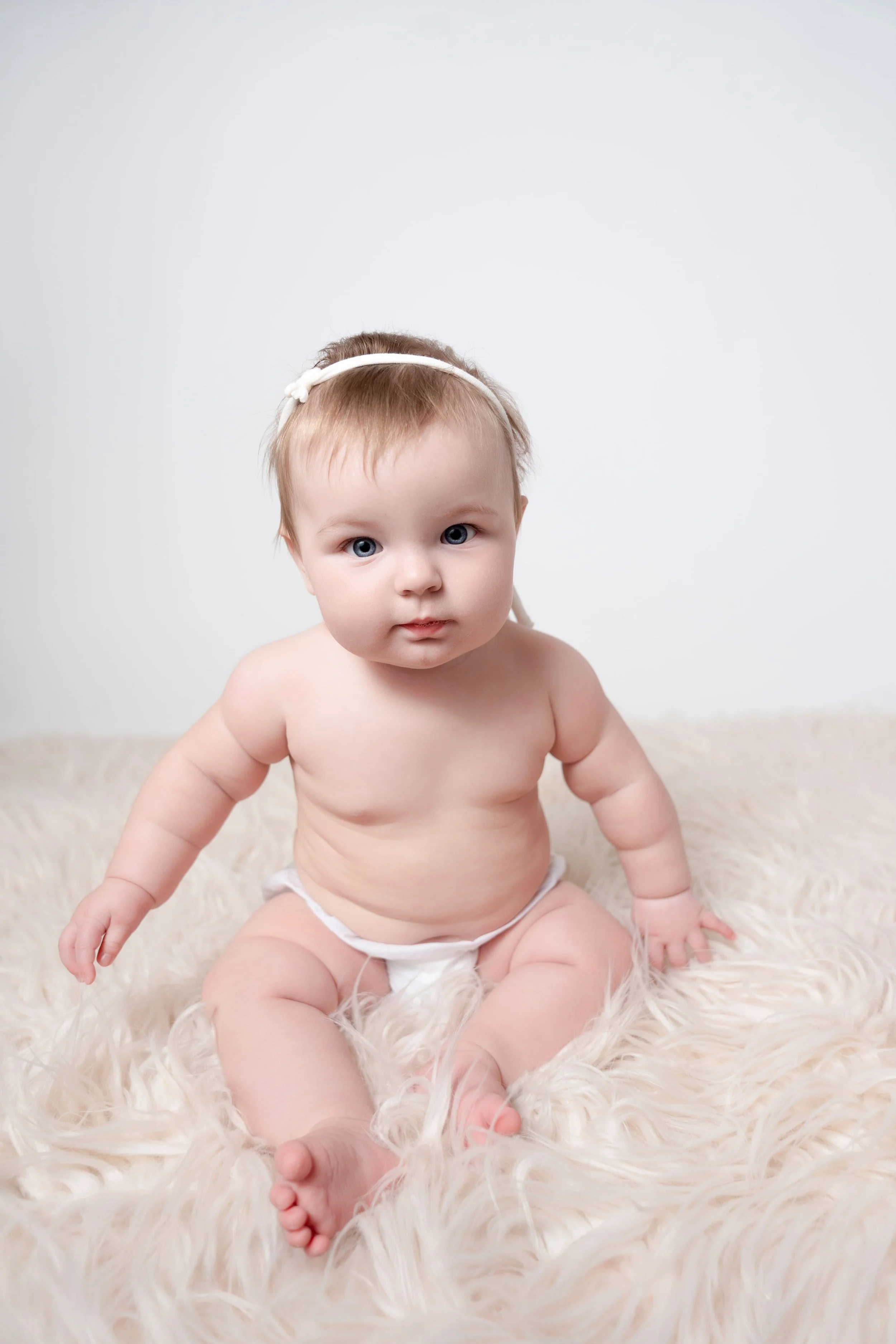 image of baby sitting in a diaper cover on a cream colored fur in a photography studio in Canton, GA