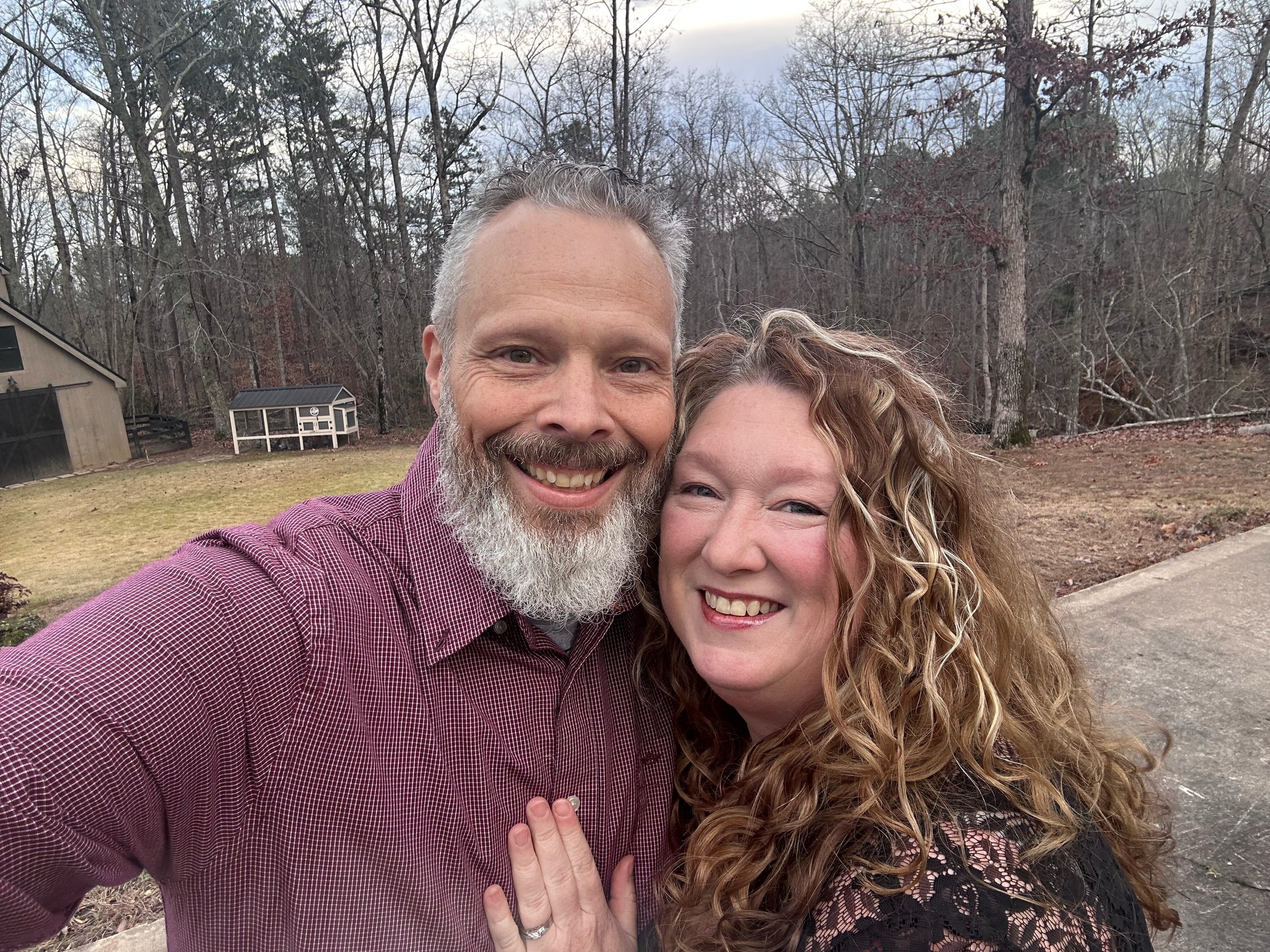 image of Cindy and her husband standing outside with view of their barn and chicken coop in back