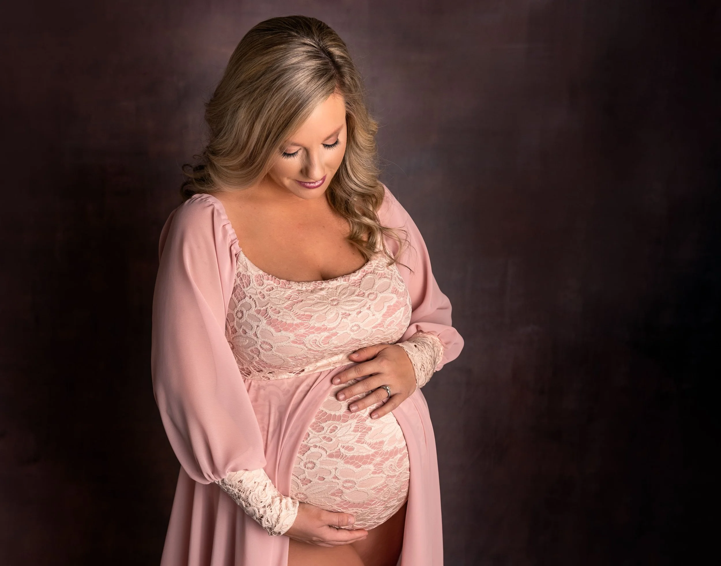 studio portrait of expectant mother in a soft pink gown highlighting her pregnant belly