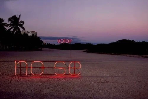Neon sign spelling out 'hope' on a sandy beach at dusk with palm trees and a purple sky.