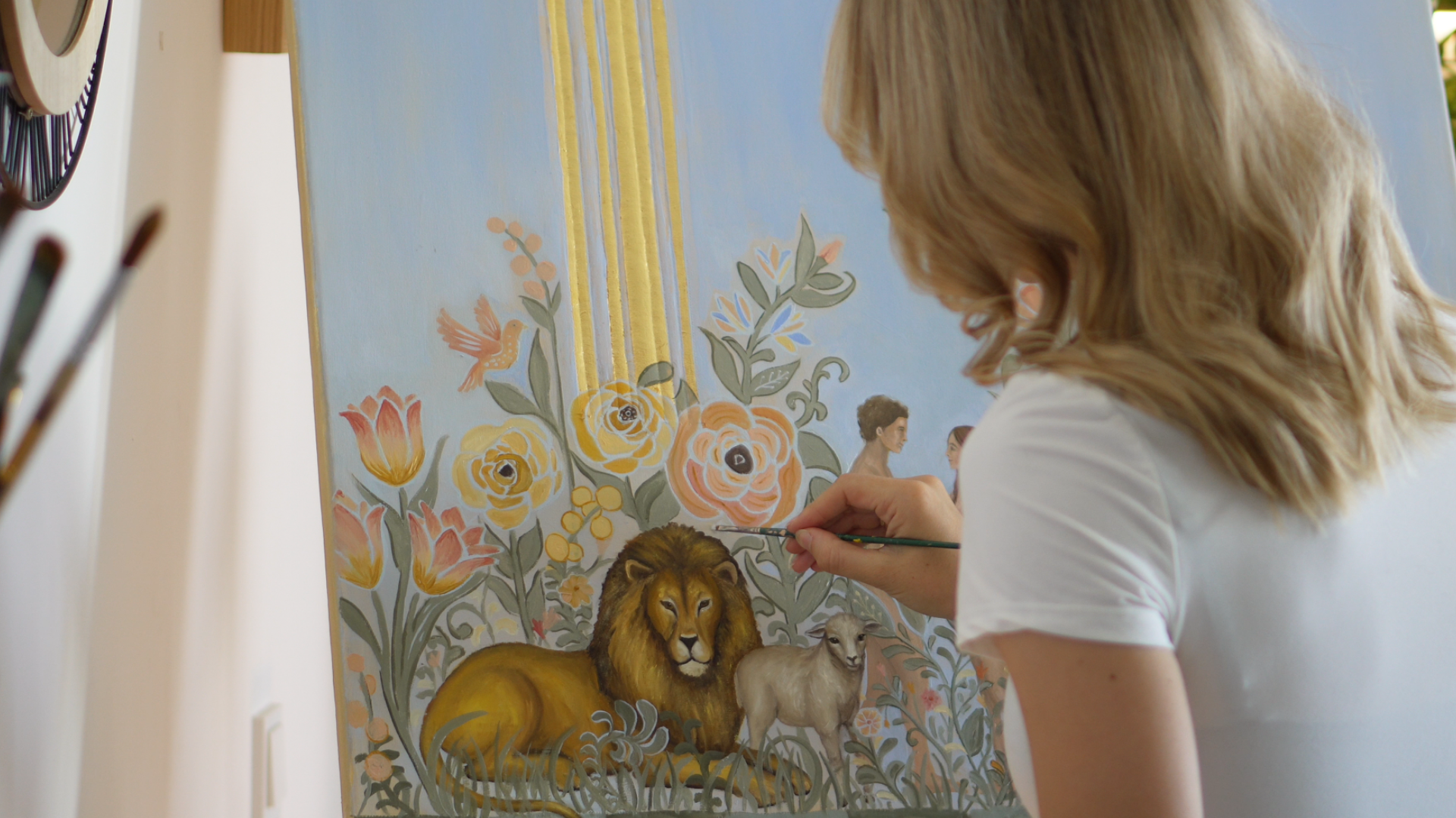 Natalie Ingerle malt im Atelier an einem christlichen Gemälde mit Blumen sowie Löwe und Lamm.