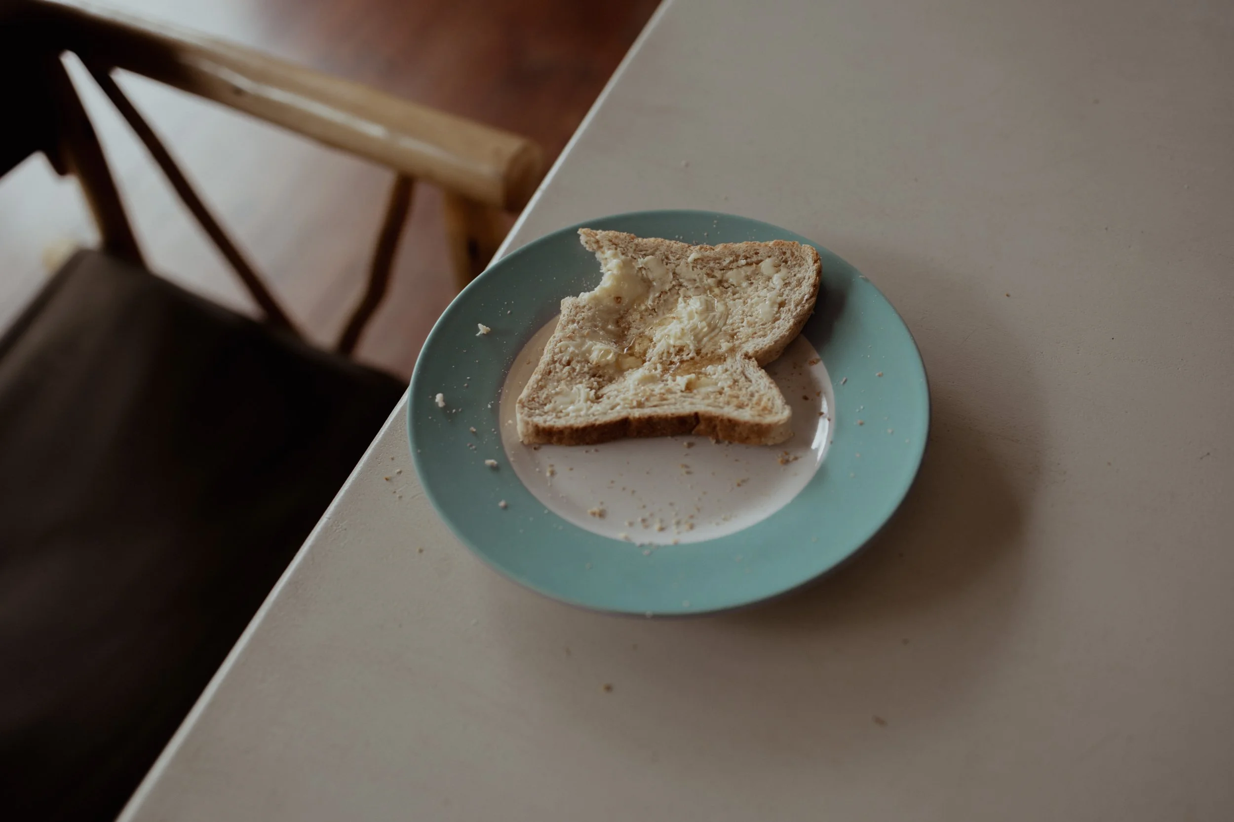 Halb gegessene Scheibe Brot mit Butter auf einem blauen Teller auf einem weißen Tisch