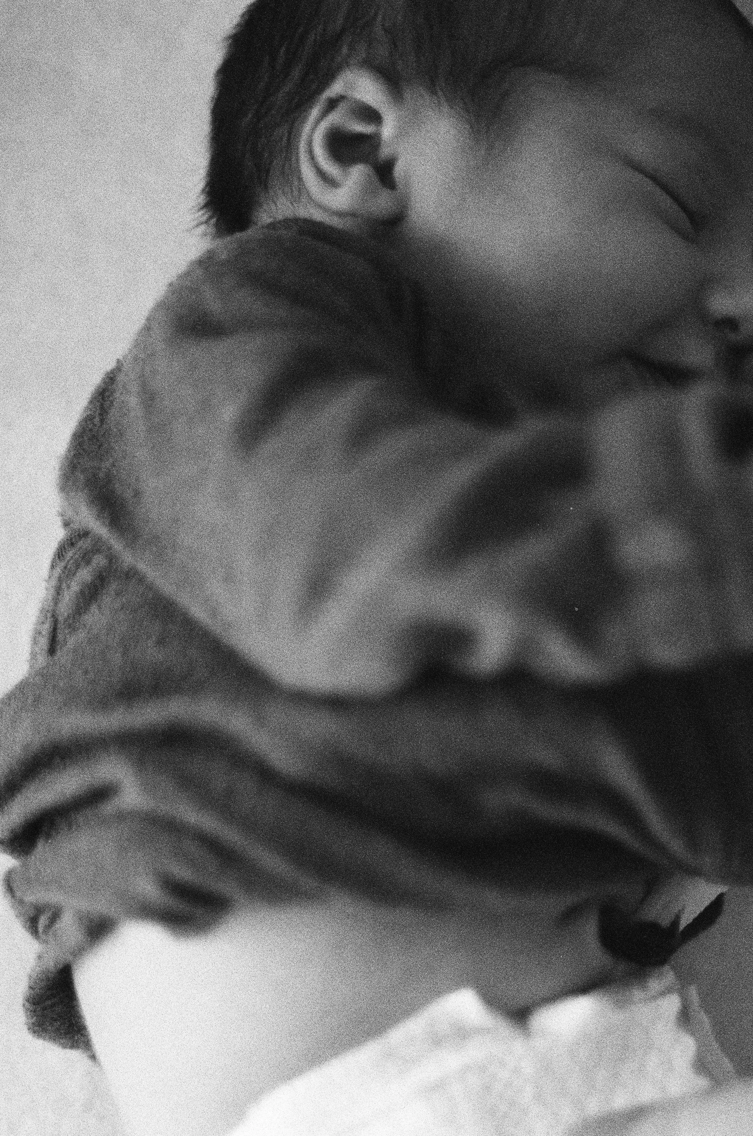 Ein sehr nahes, schwarzes und weißes Foto eines schlafenden Babys, das lächelt, mit geschlossenen Augen, trägt einen Pullover, mit Fokus auf das Gesicht und die Kleidung.