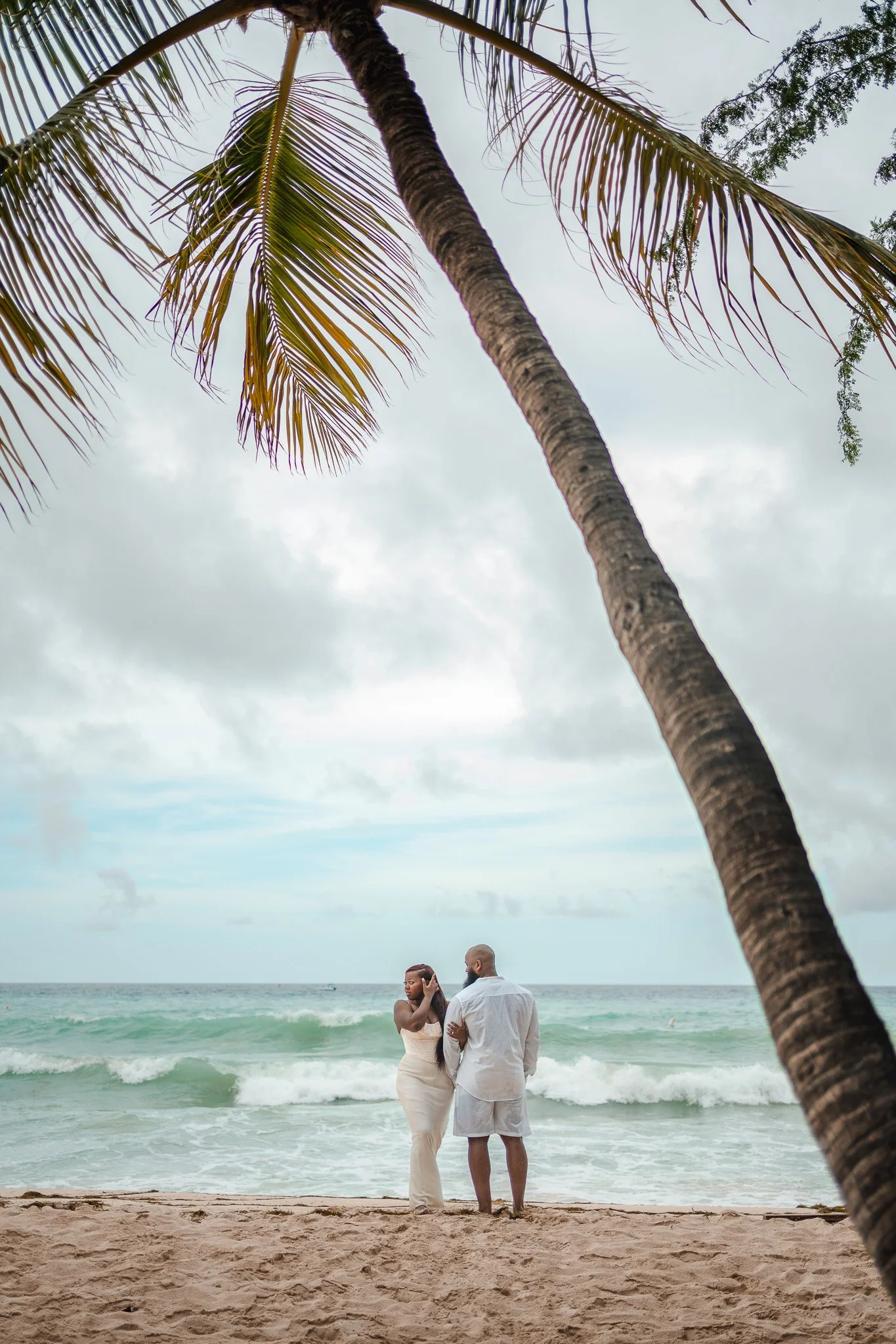 Couple embracing on a tropical beach under a leaning palm tree